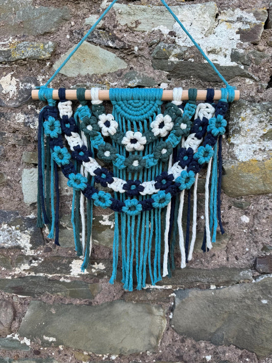 Decorative wall hanging with macrame flowers and fringes on a stone wall background