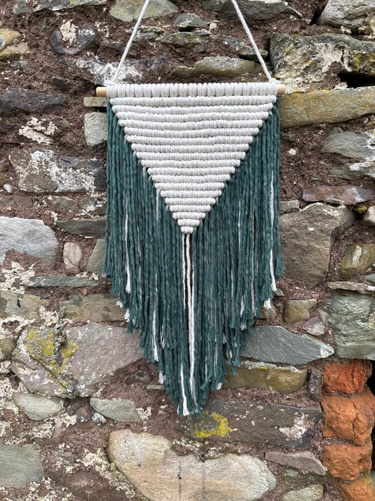 Macrame wall hanging with green and white cotton against a stone wall.