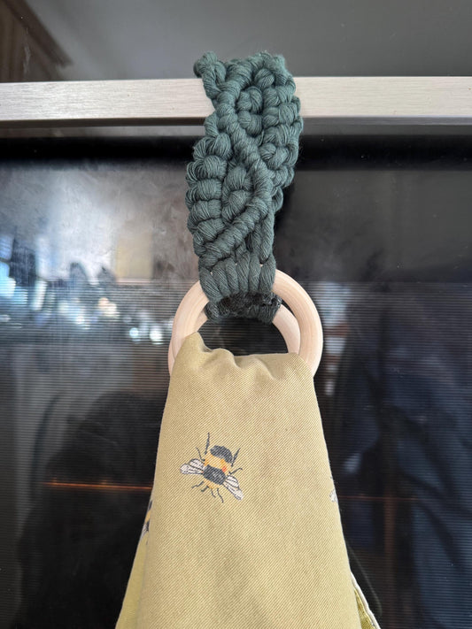 green macrame attached to wooden rings holding a yellow tea towel with a bee design