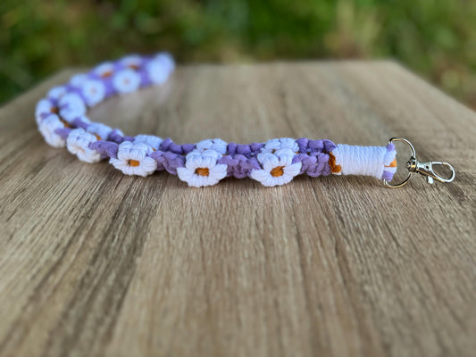 Handmade macrame lanyard with purple and white floral pattern on a wooden surface