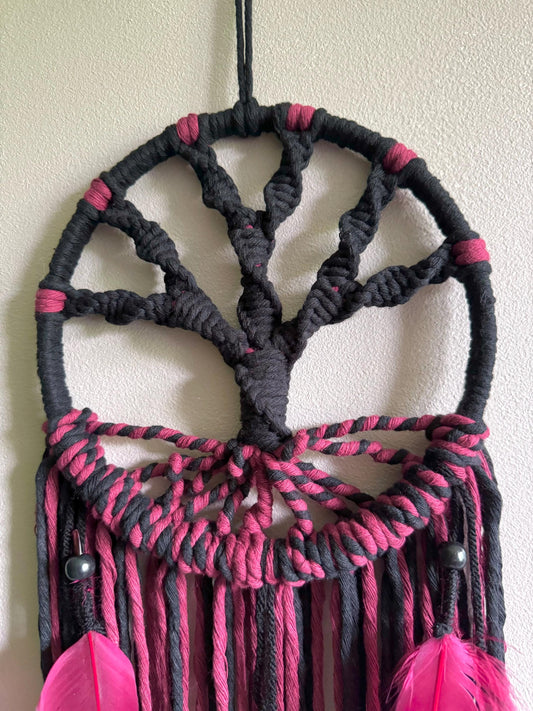 Black and pink macrame wall hanging with feathers against a beige wall.