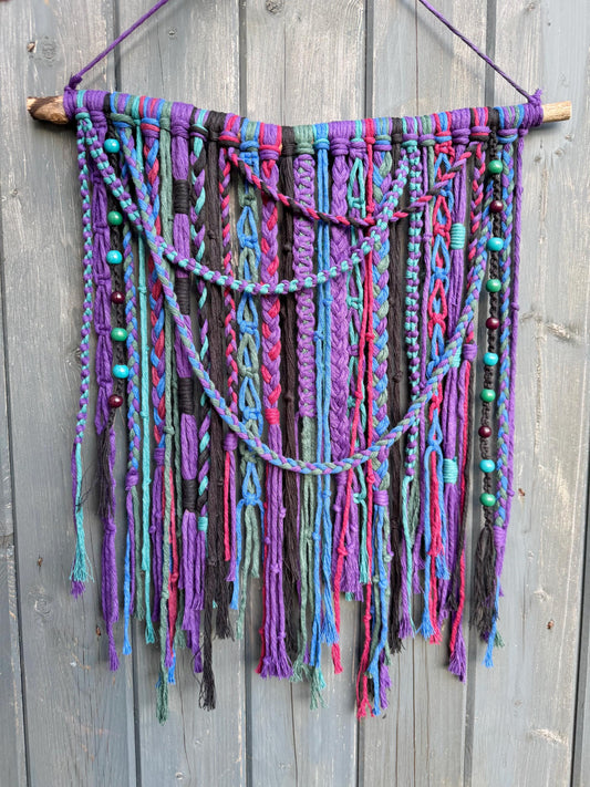 Colorful knotted wall hanging with beads on a wooden background