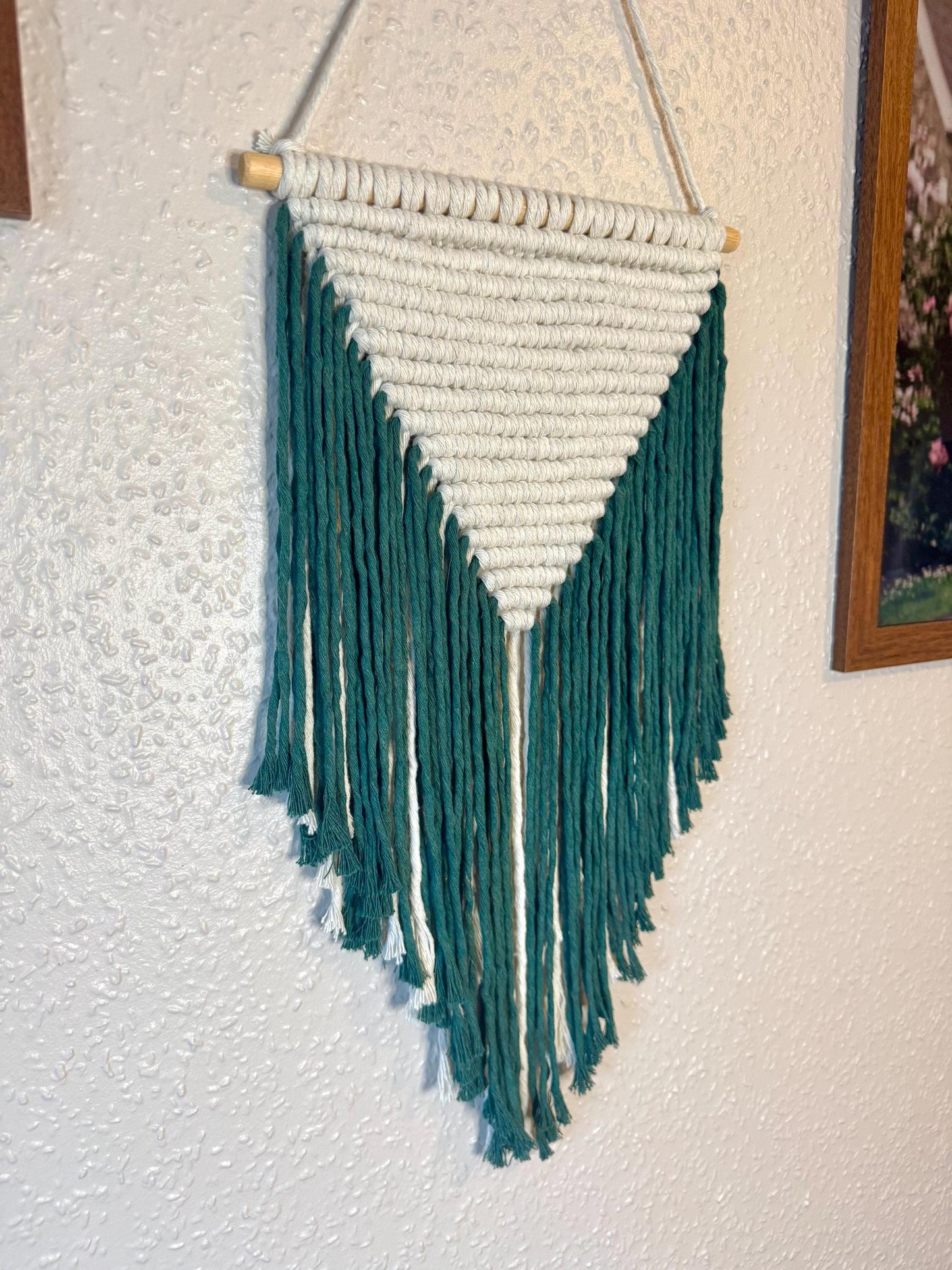 Macrame wall hanging with green and white yarn on a plain wall.