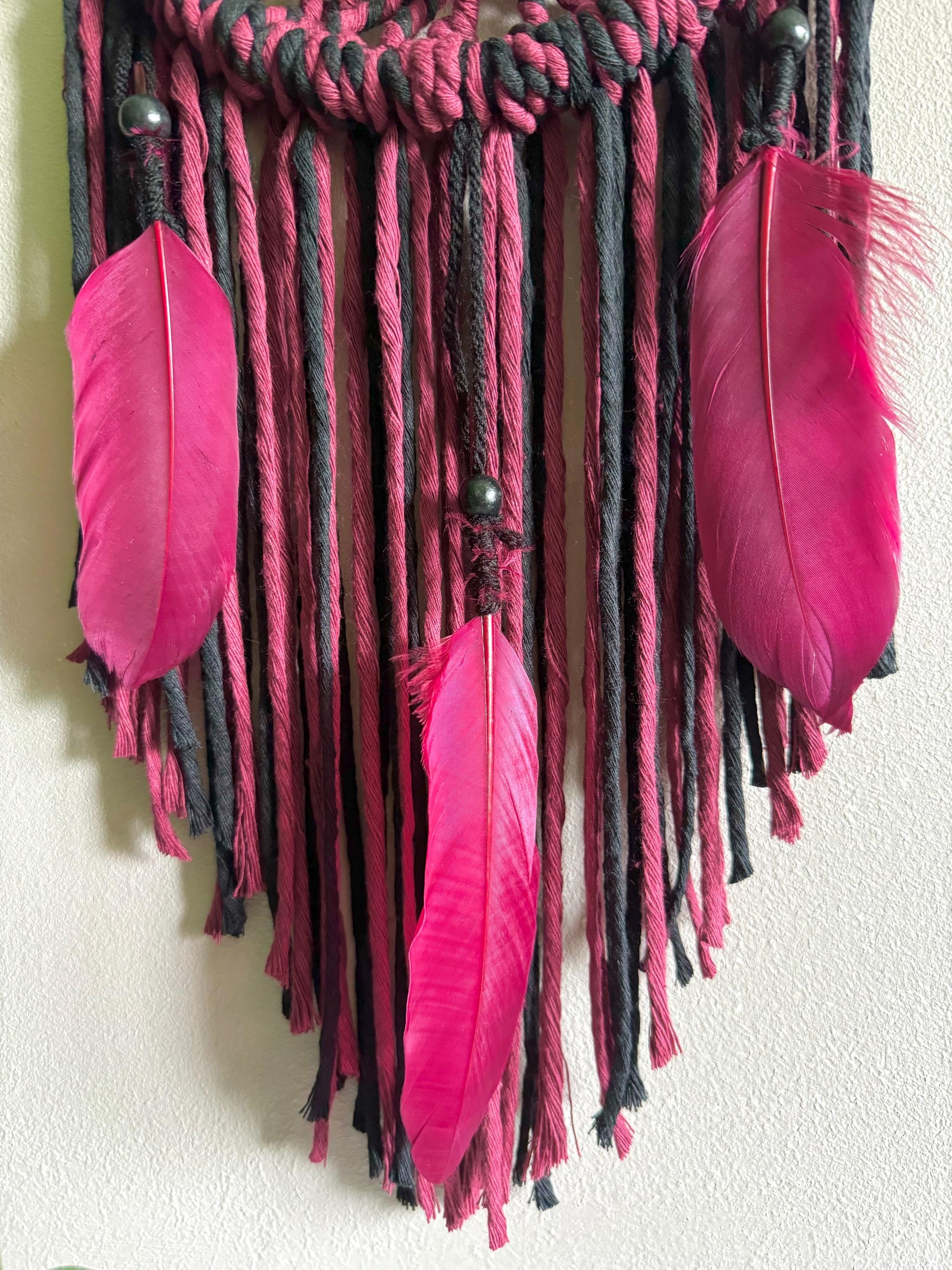 Decorative wall hanging with pink feathers and braided strings on a plain background