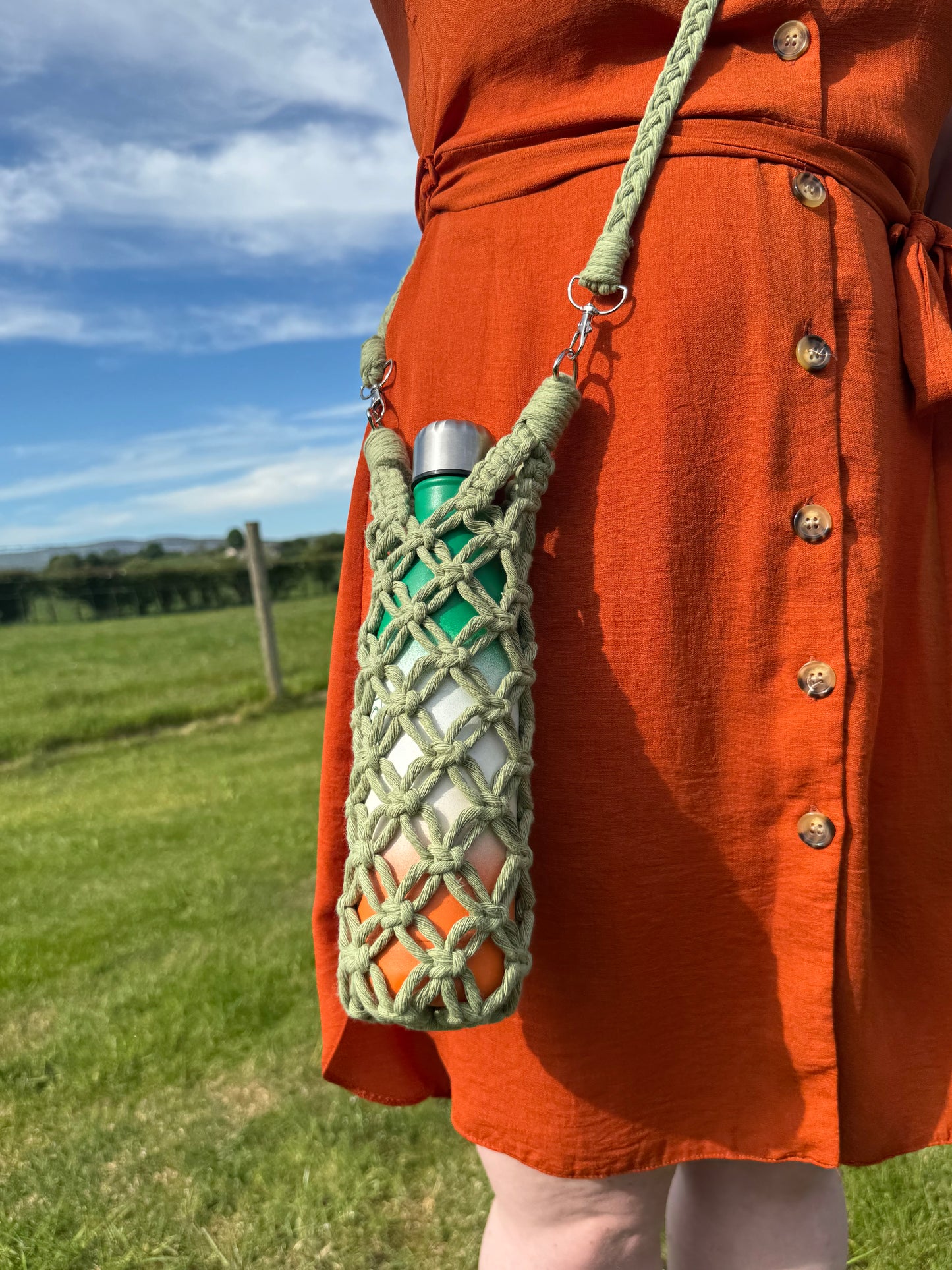 Green macrame pouch with a metal clip and a braided strap on an orange jacket against a blurred outdoor background