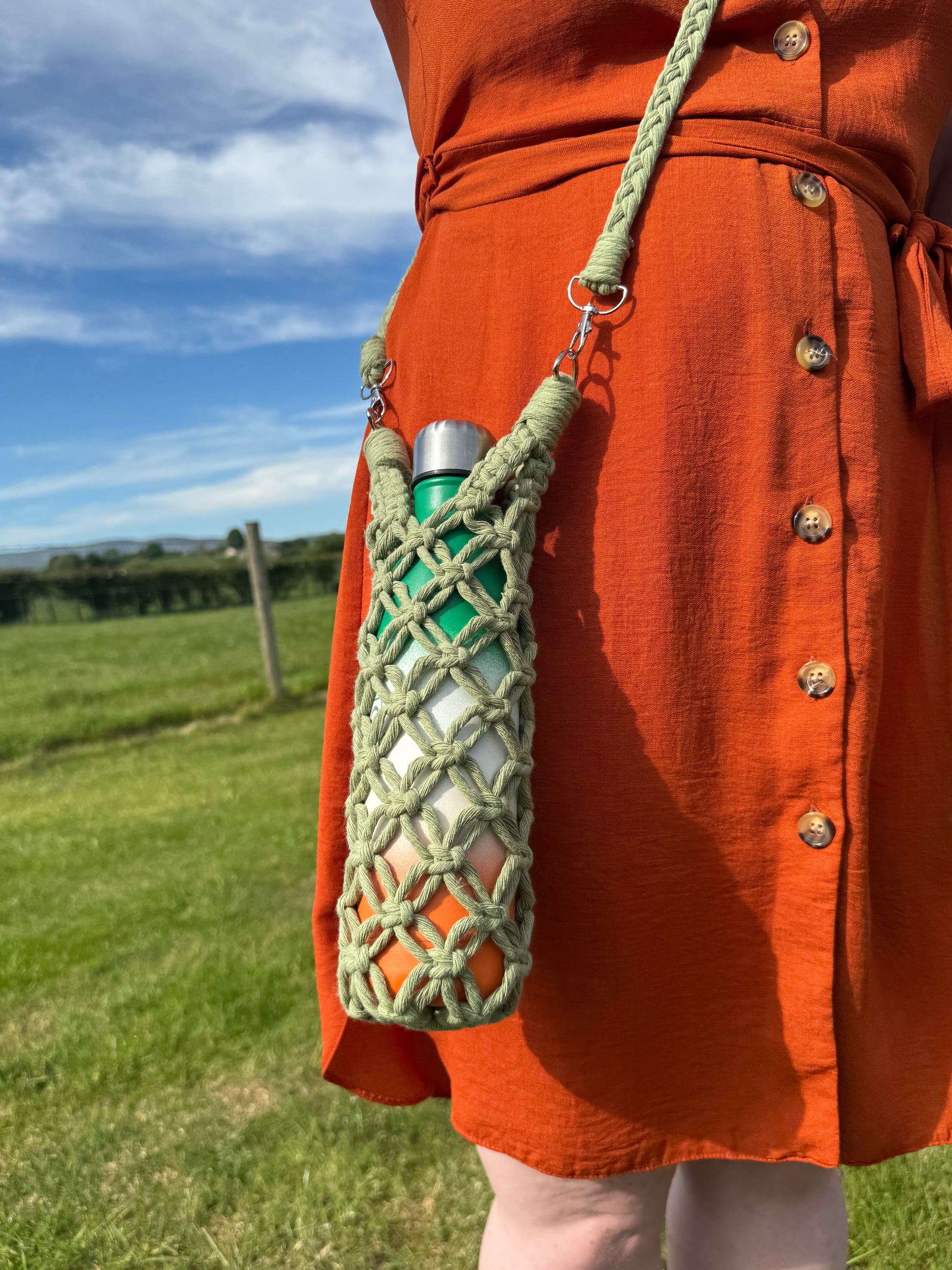 Green macrame pouch with a metal clip and a braided strap on an orange jacket against a blurred outdoor background