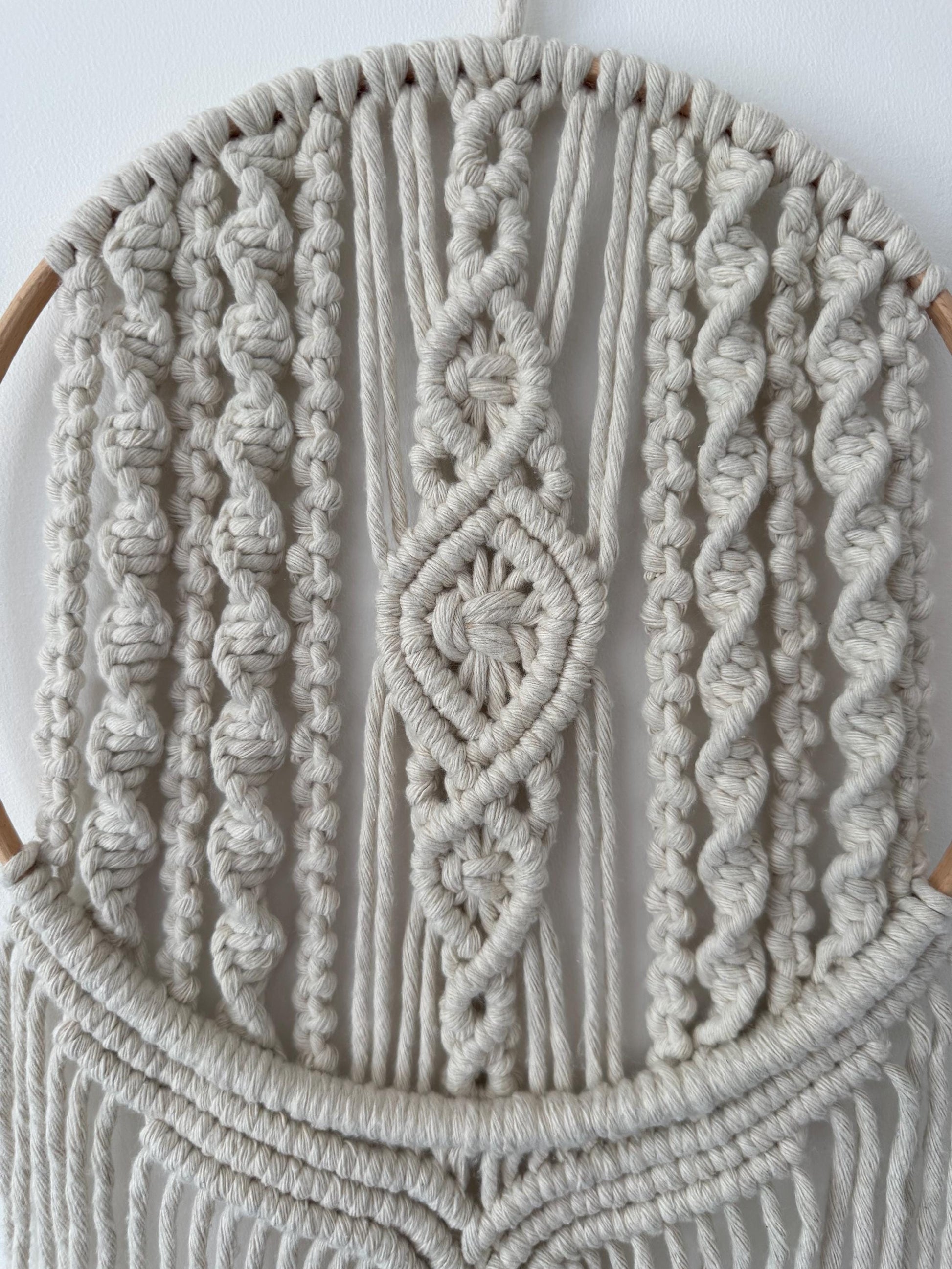 Close-up of a macrame wall hanging with intricate patterns on a white background