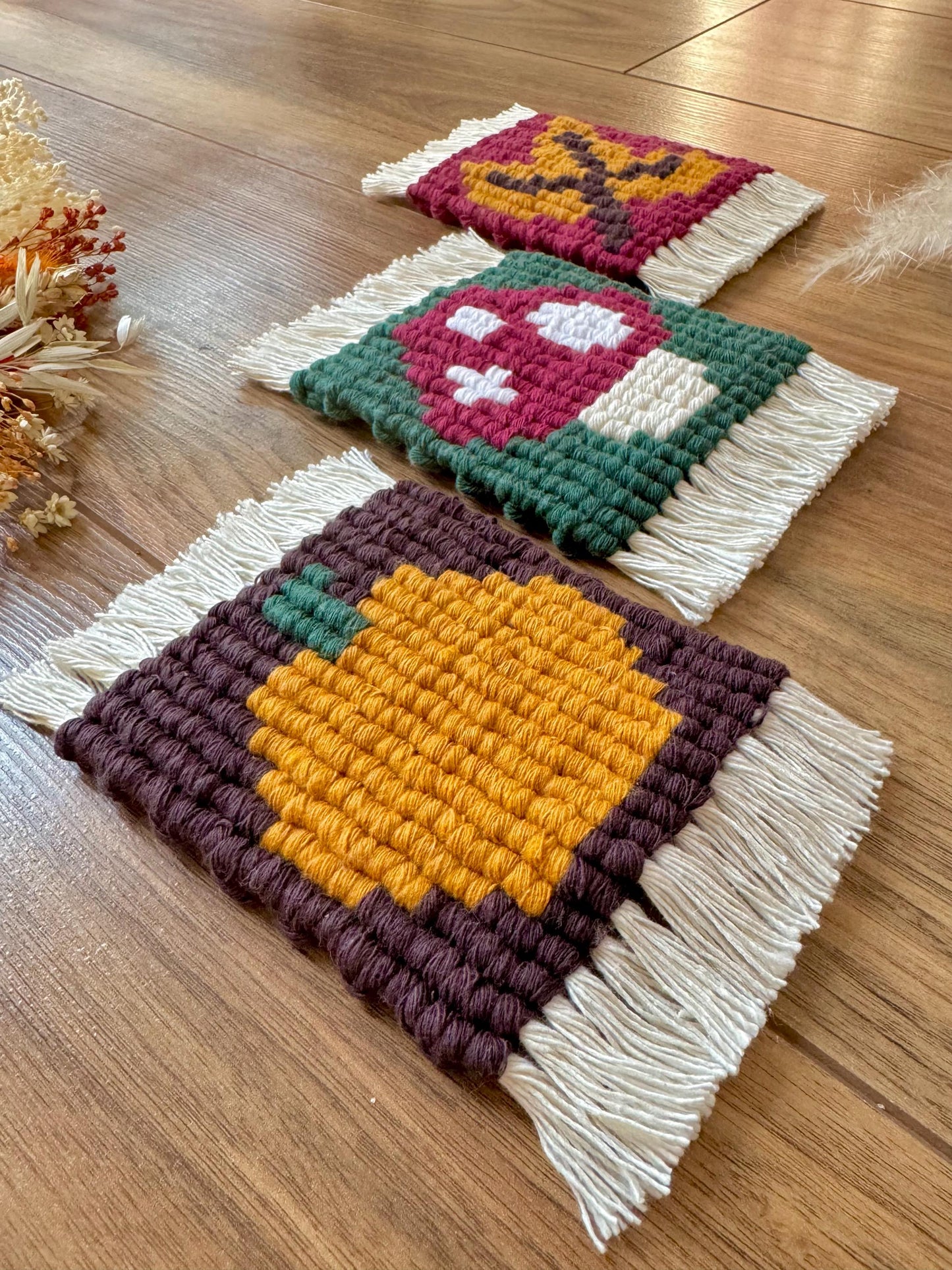 Three macrame coasters with colorful patterns on a wooden surface.