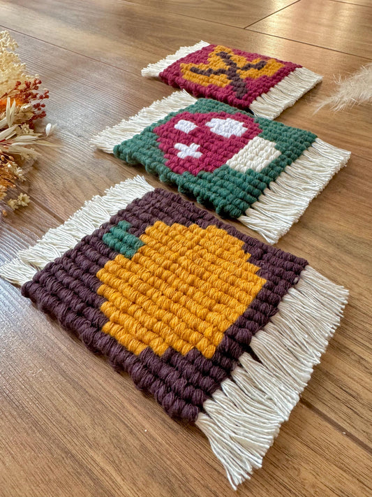 Three macrame coasters with colorful patterns on a wooden surface.