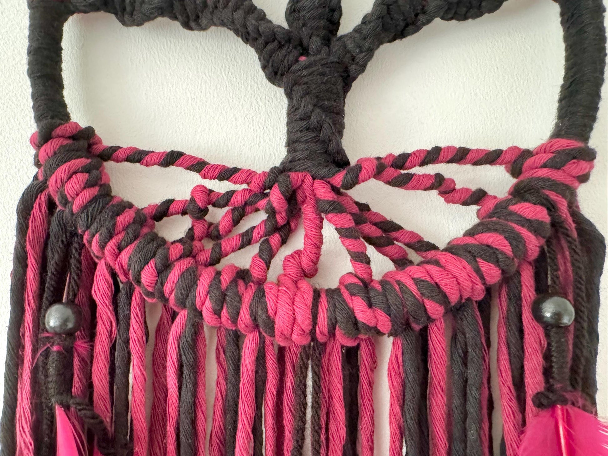 Macrame wall hanging with pink and black strings on a white background