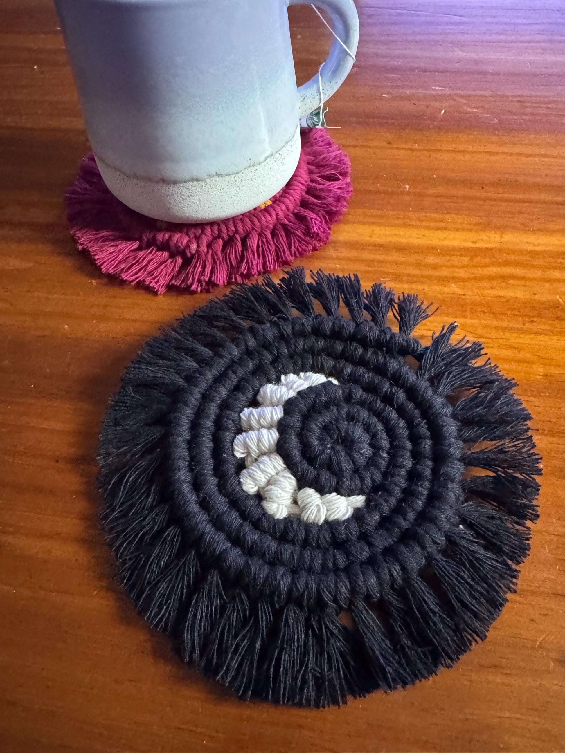 Black and white woven coaster with pink fringed coaster on a wooden surface