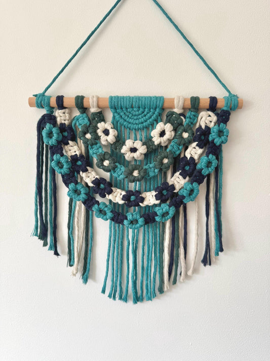 Macrame wall hanging with blue floral patterns and fringes on a white background