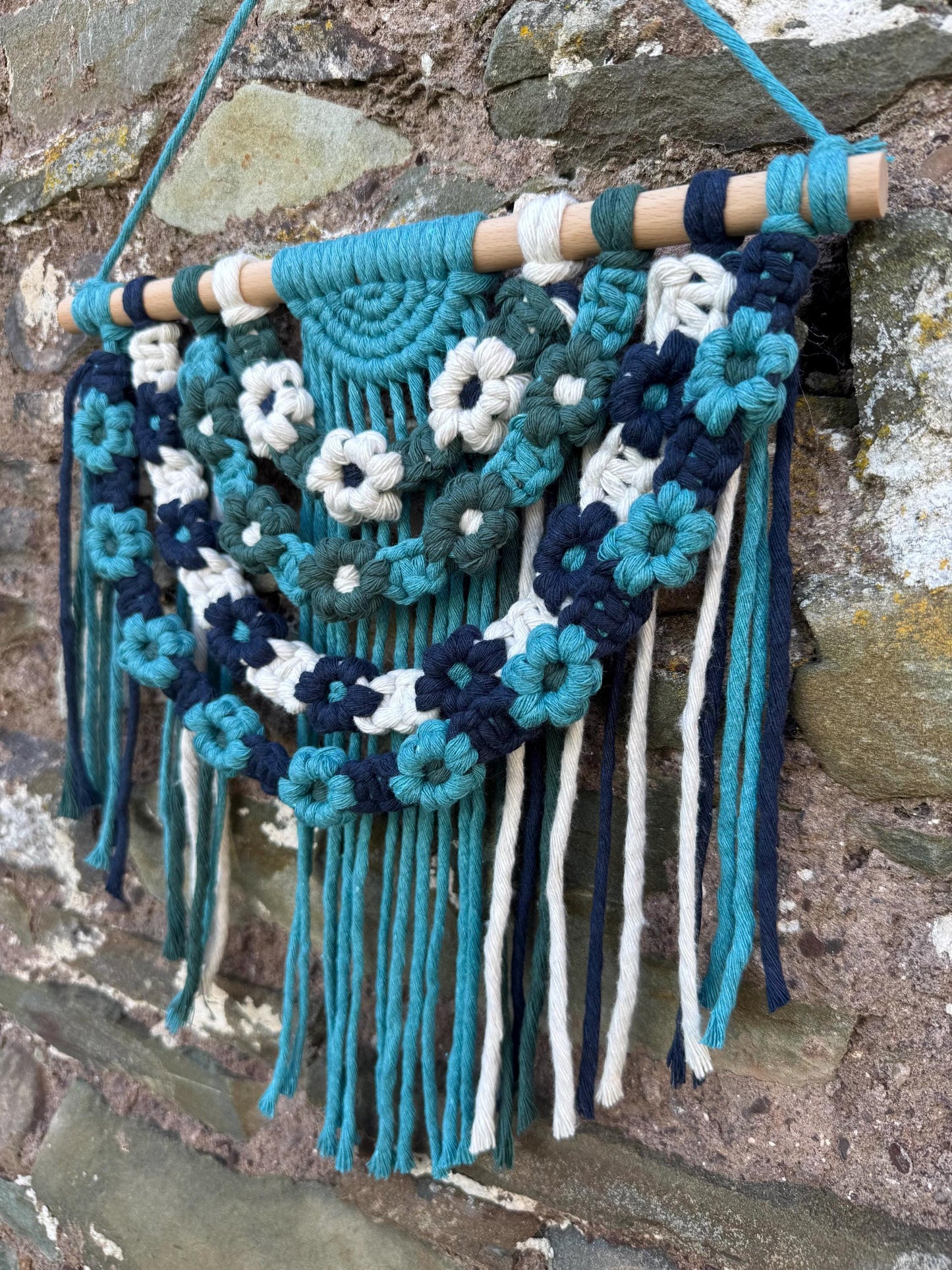 Decorative wall hanging with floral patterns and fringes on a stone wall background