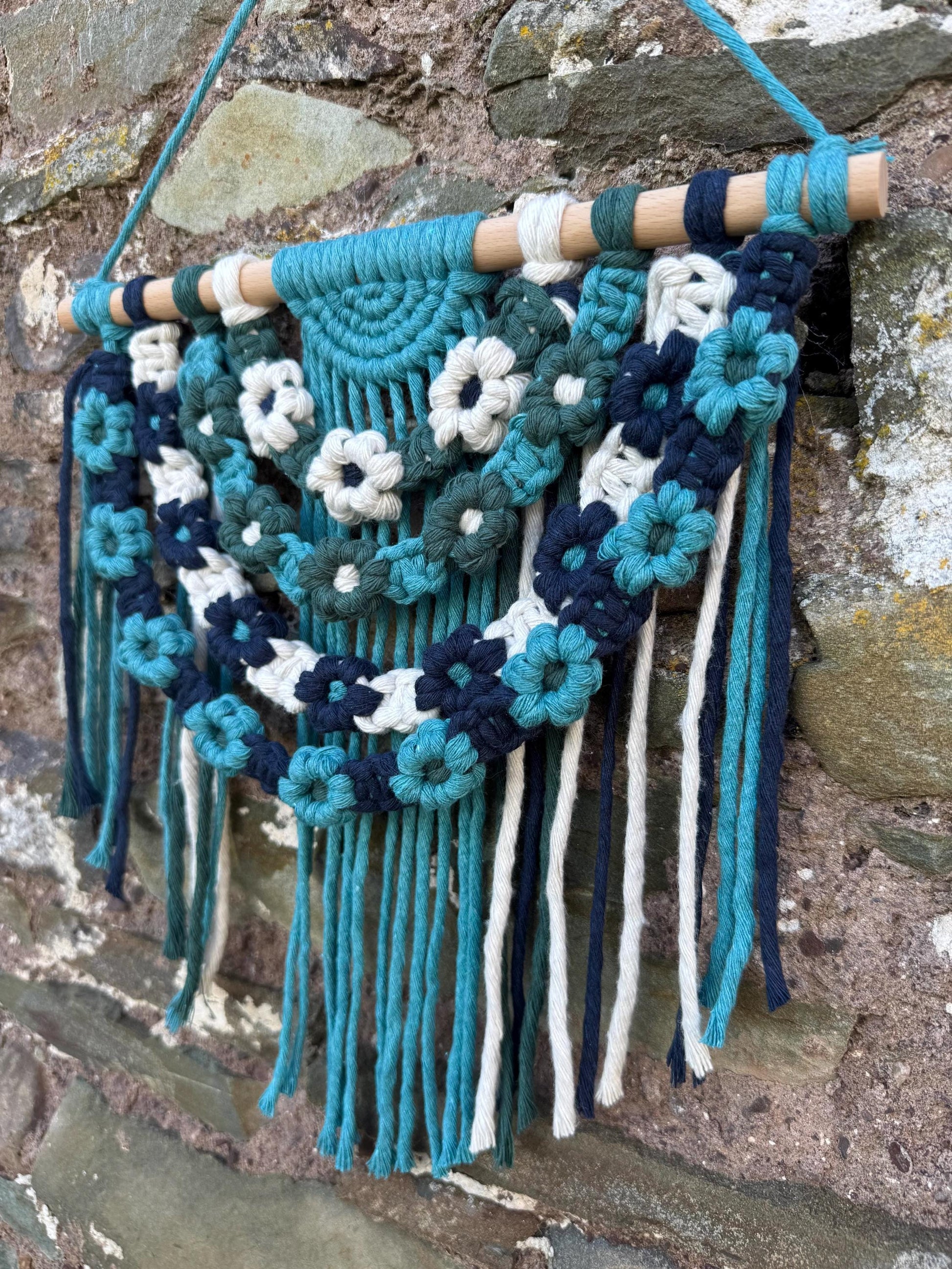 Decorative wall hanging with floral patterns and fringes on a stone wall background