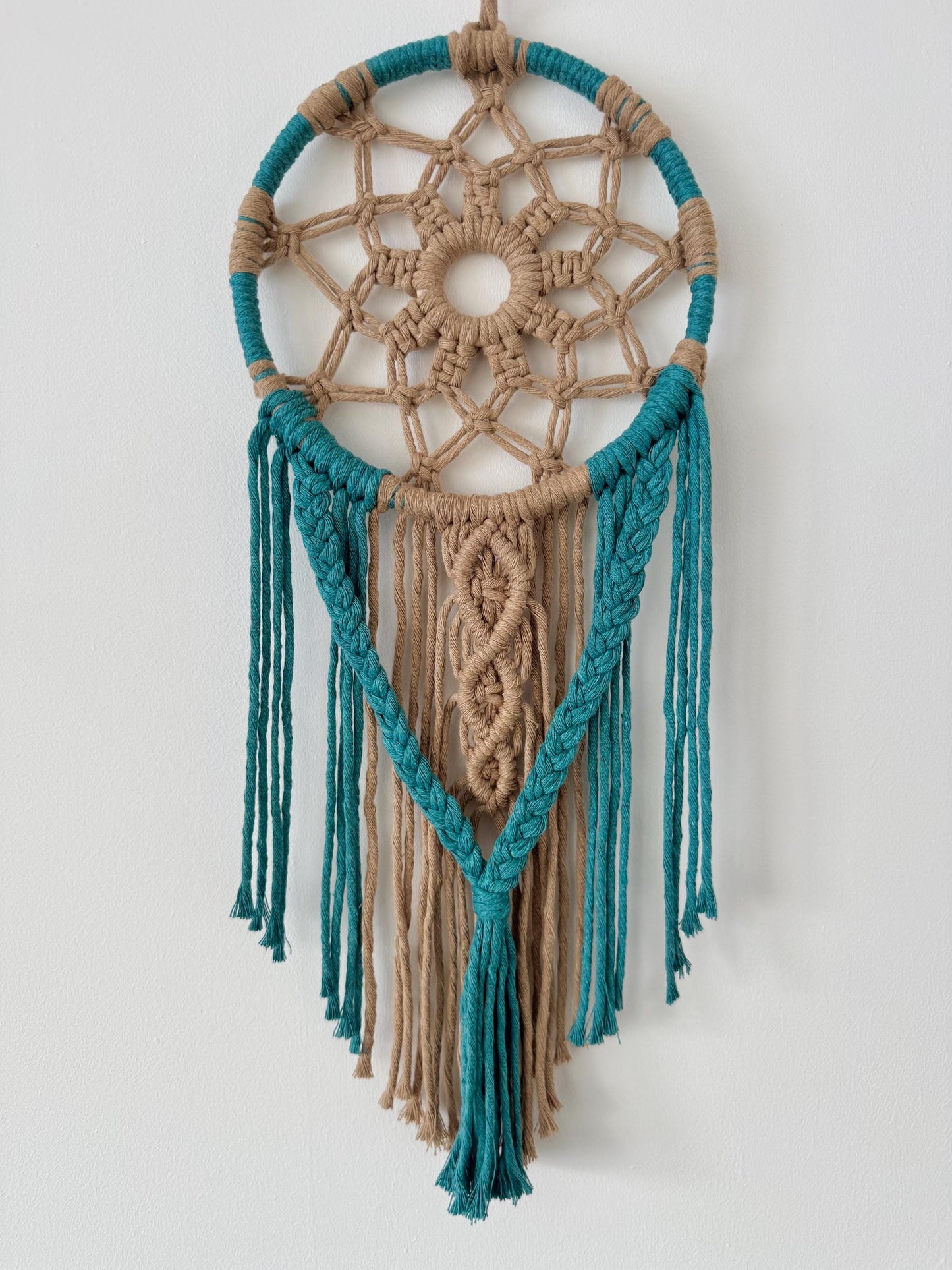 Macrame wall hanging with teal and beige colors on a white background