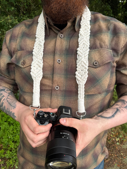 Person holding a camera with a white boho macrame strap outdoors