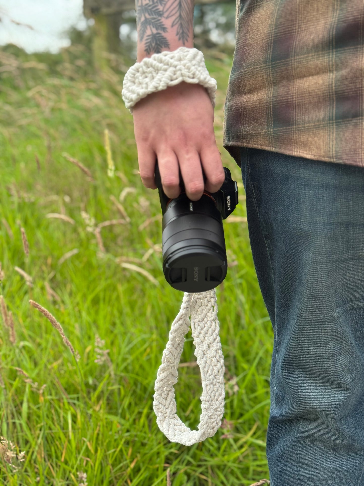 Person holding a camera with a white strap attached, standing in a grassy field.