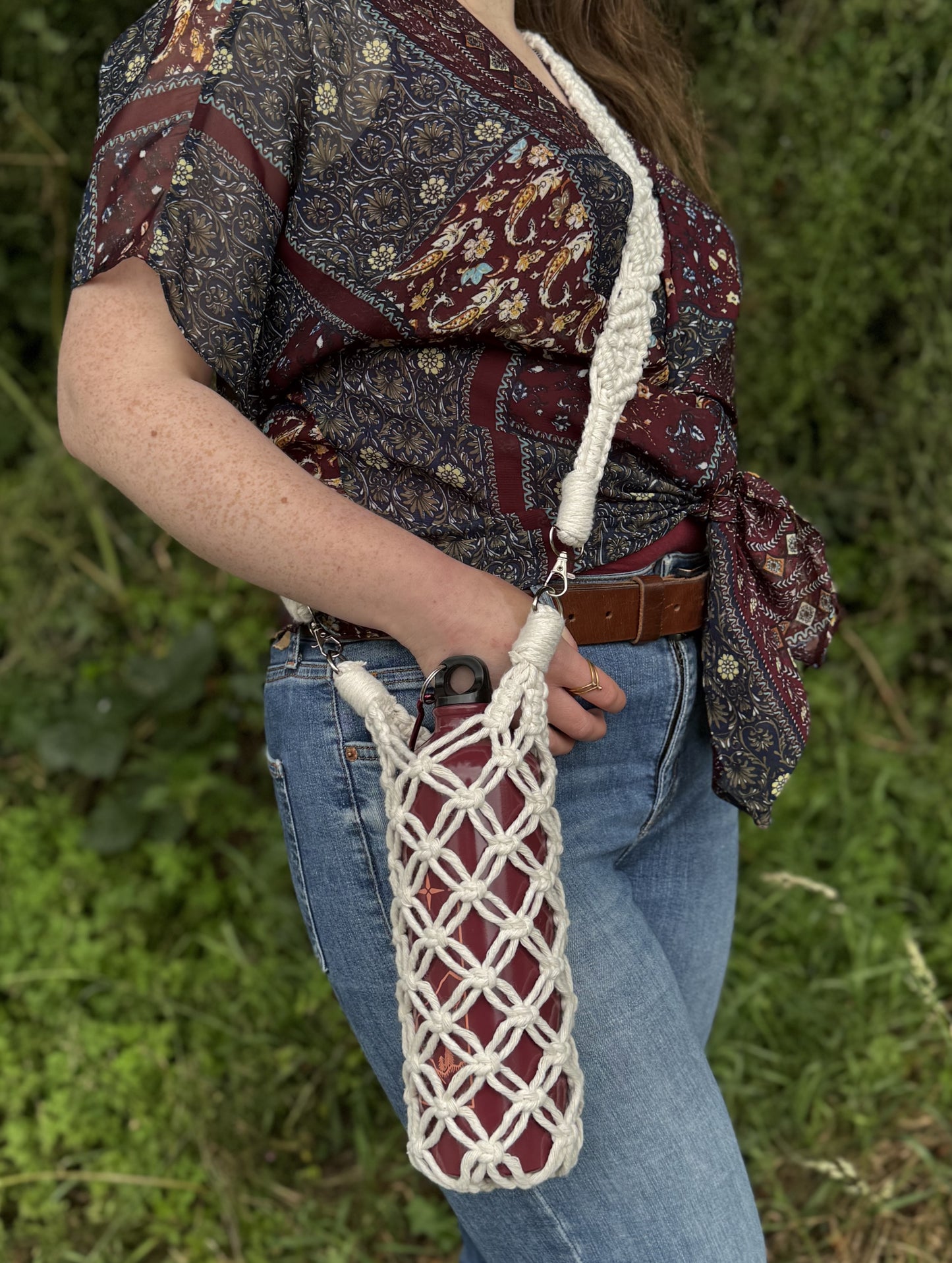 Person holding a woven bag with a patterned shawl over shoulders against a natural background