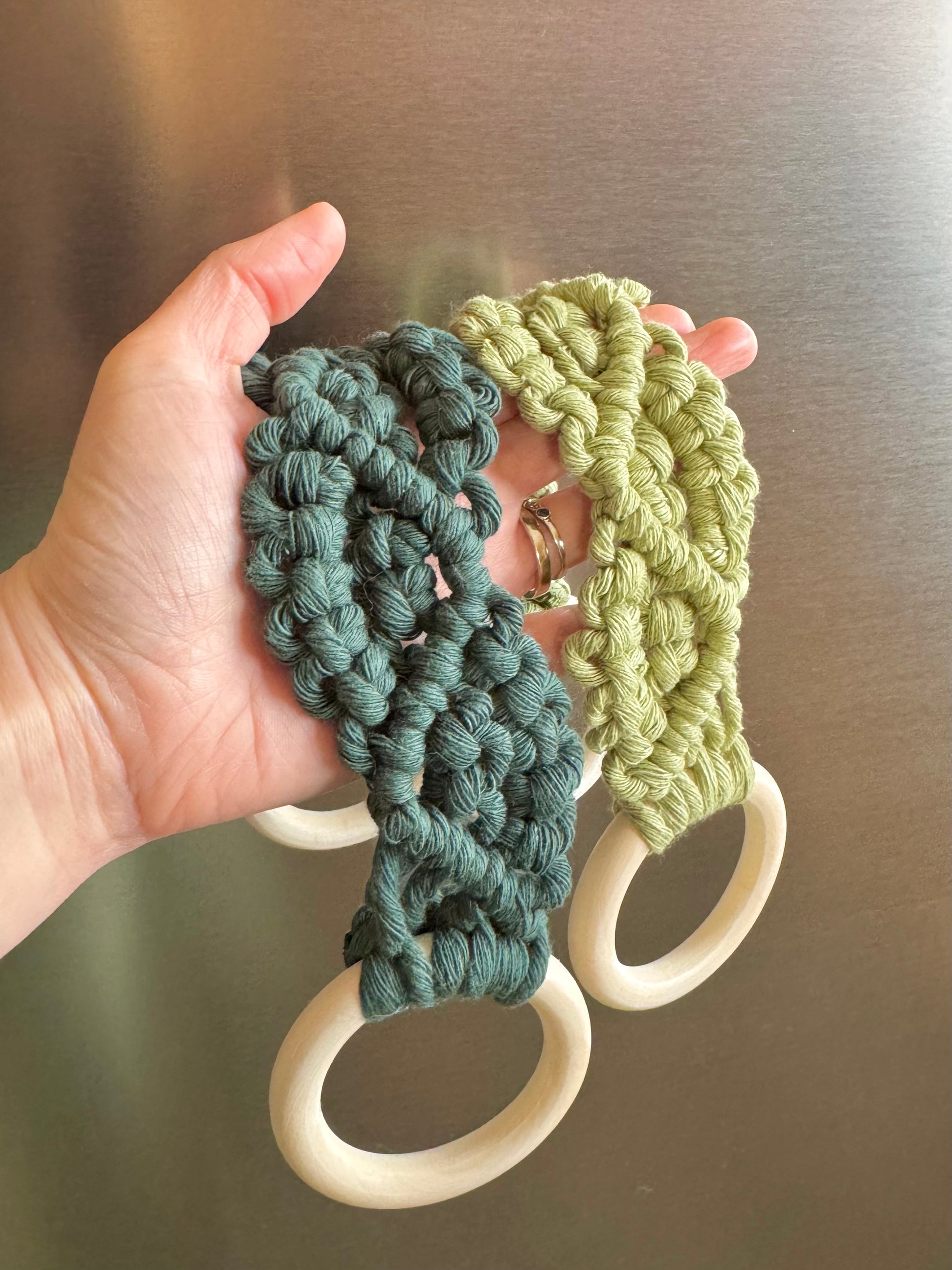 Hand holding two macrame kitchen towel holders with wooden rings