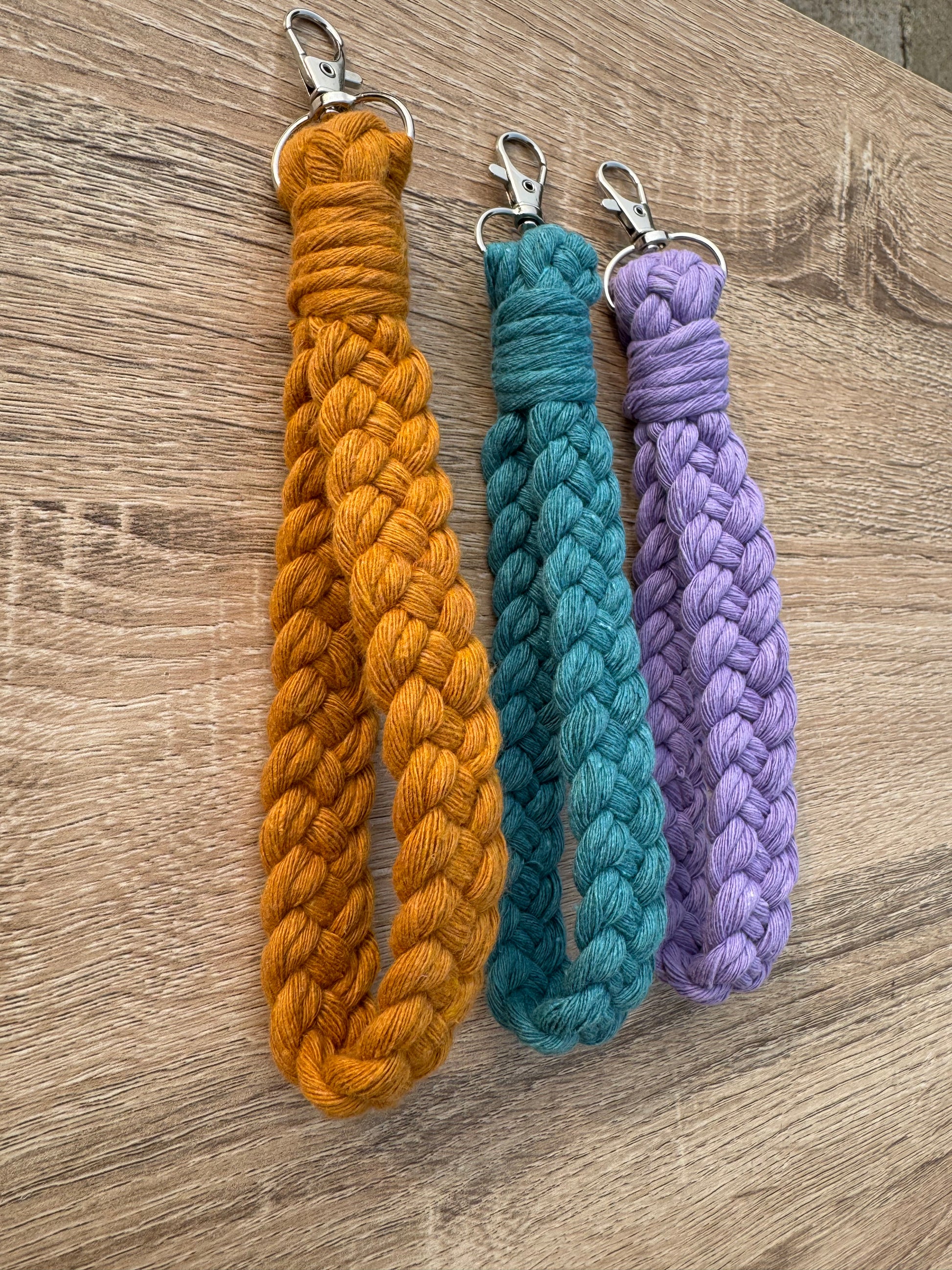 Three braided wristlets in purple, blue, and orange on a wooden surface