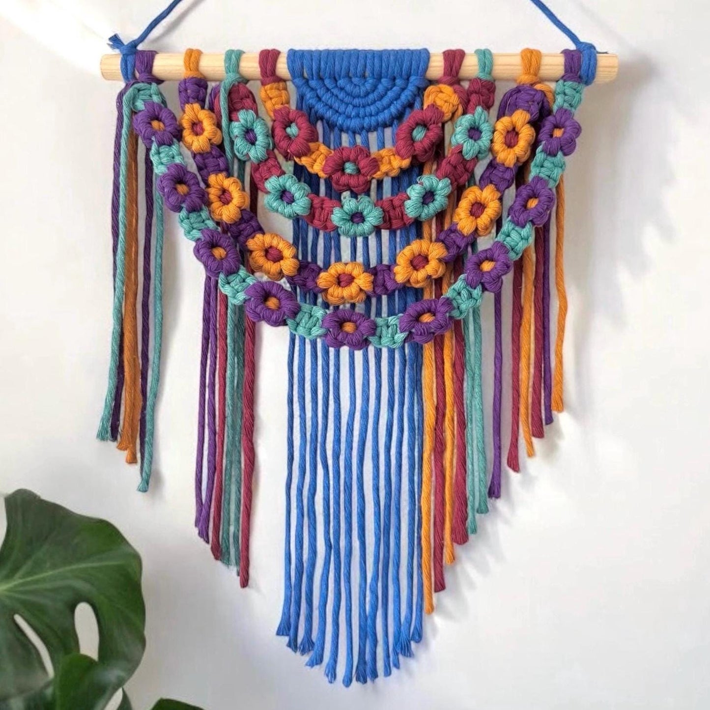 Colorful macrame wall hanging with floral patterns on a white background