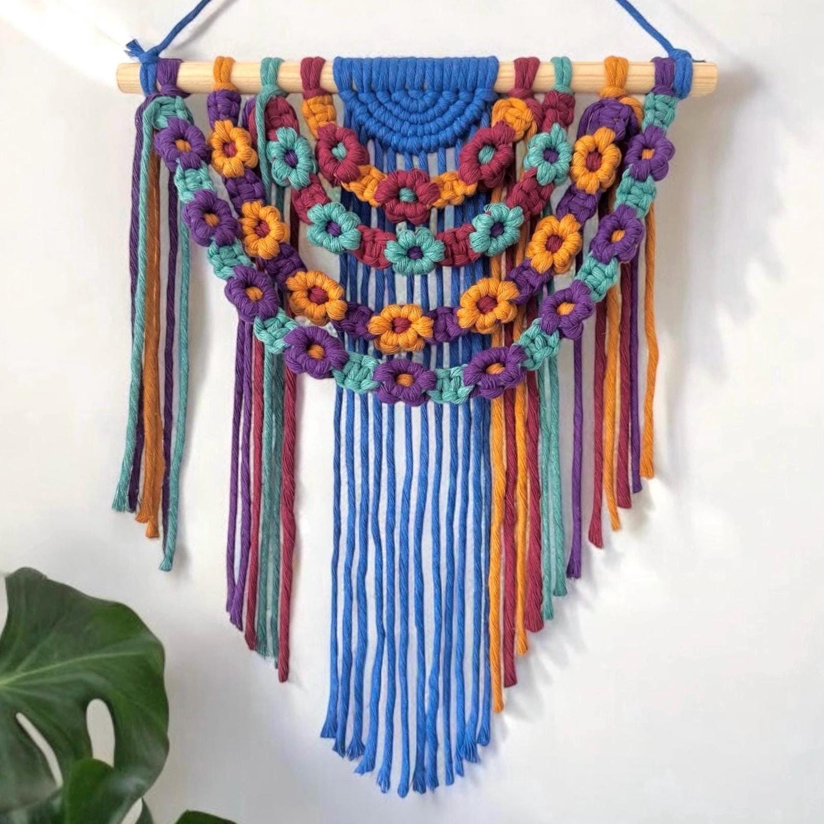 Colorful macrame wall hanging with floral patterns on a white background