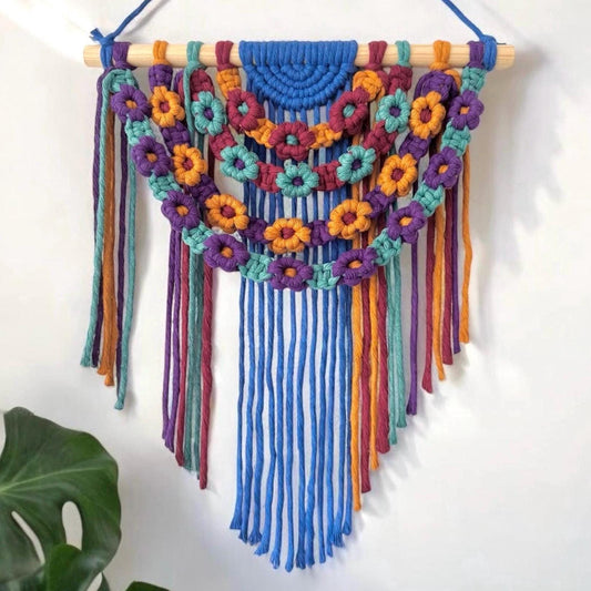 Colorful macrame wall hanging with floral patterns on a white background