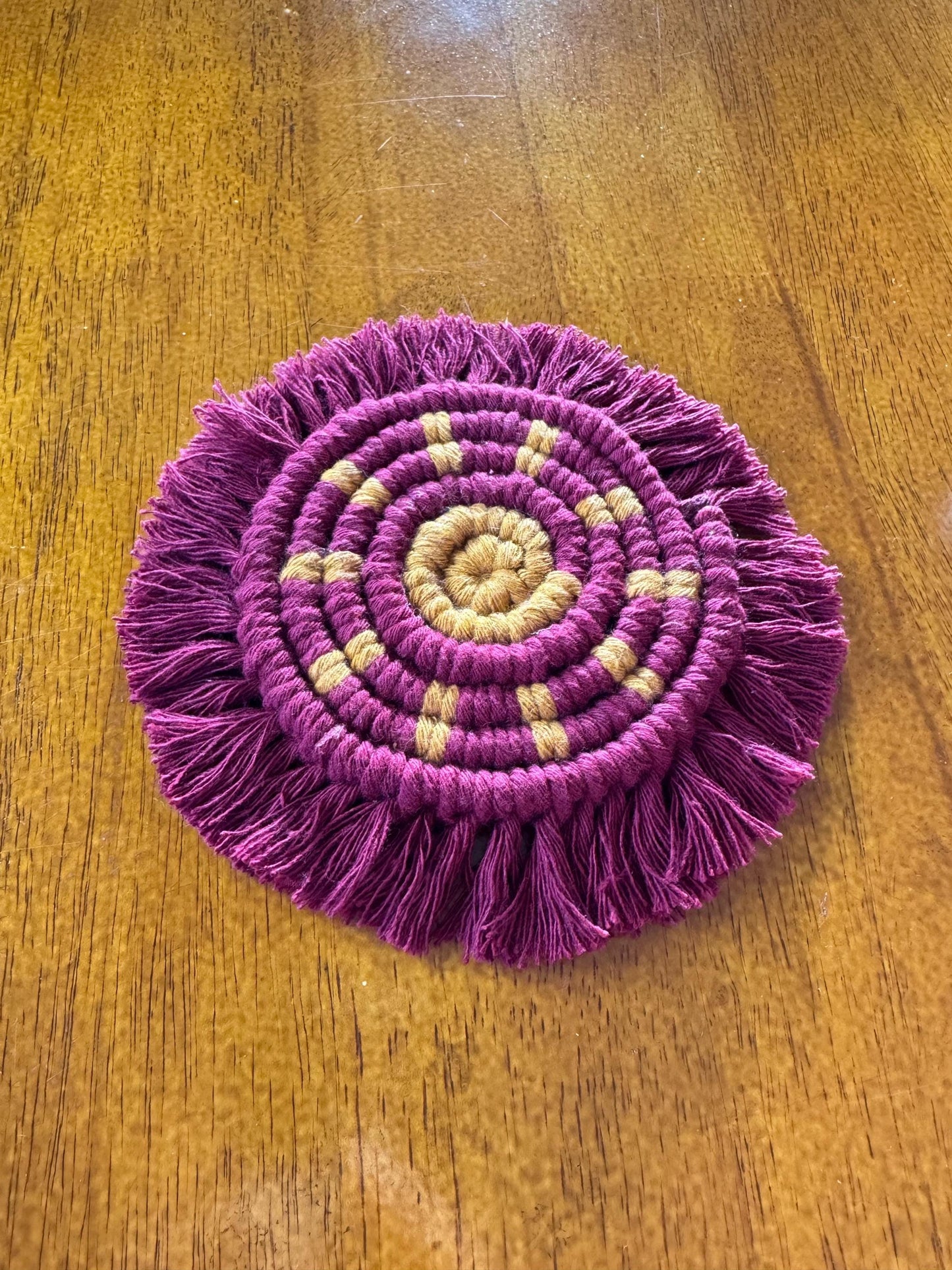 Burgundy macrame coaster with a yellow sun detail on a wooden surface