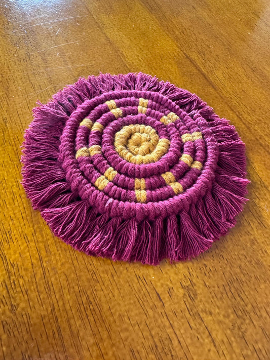burgundy and yellow macrame sun coaster on a wooden surface