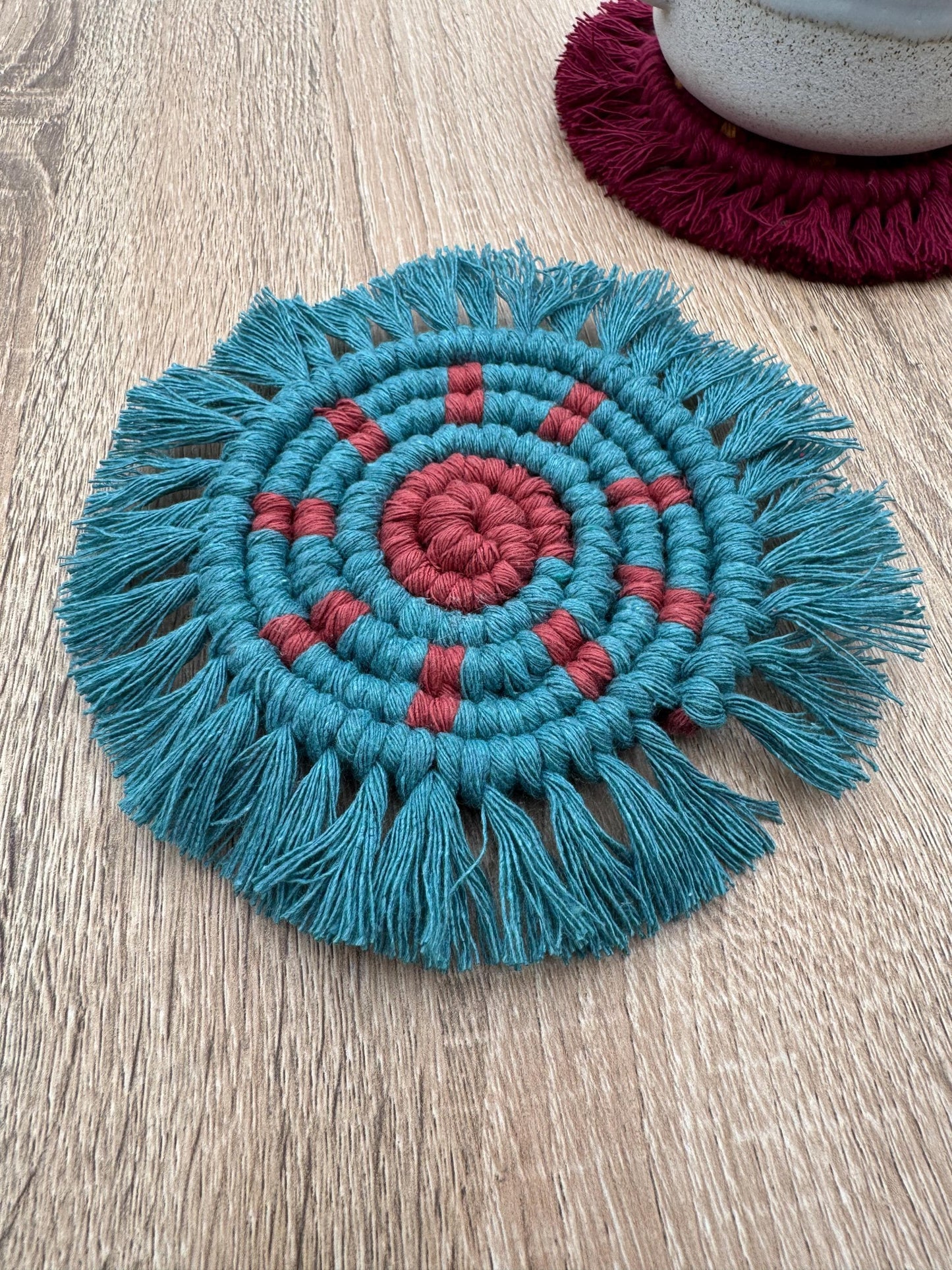Teal and red macrame coaster on a wooden surface