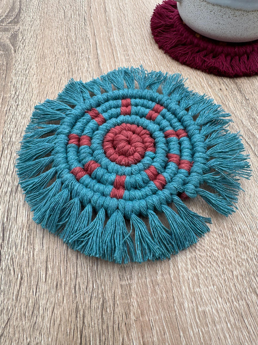 Teal and red macrame coaster on a wooden surface