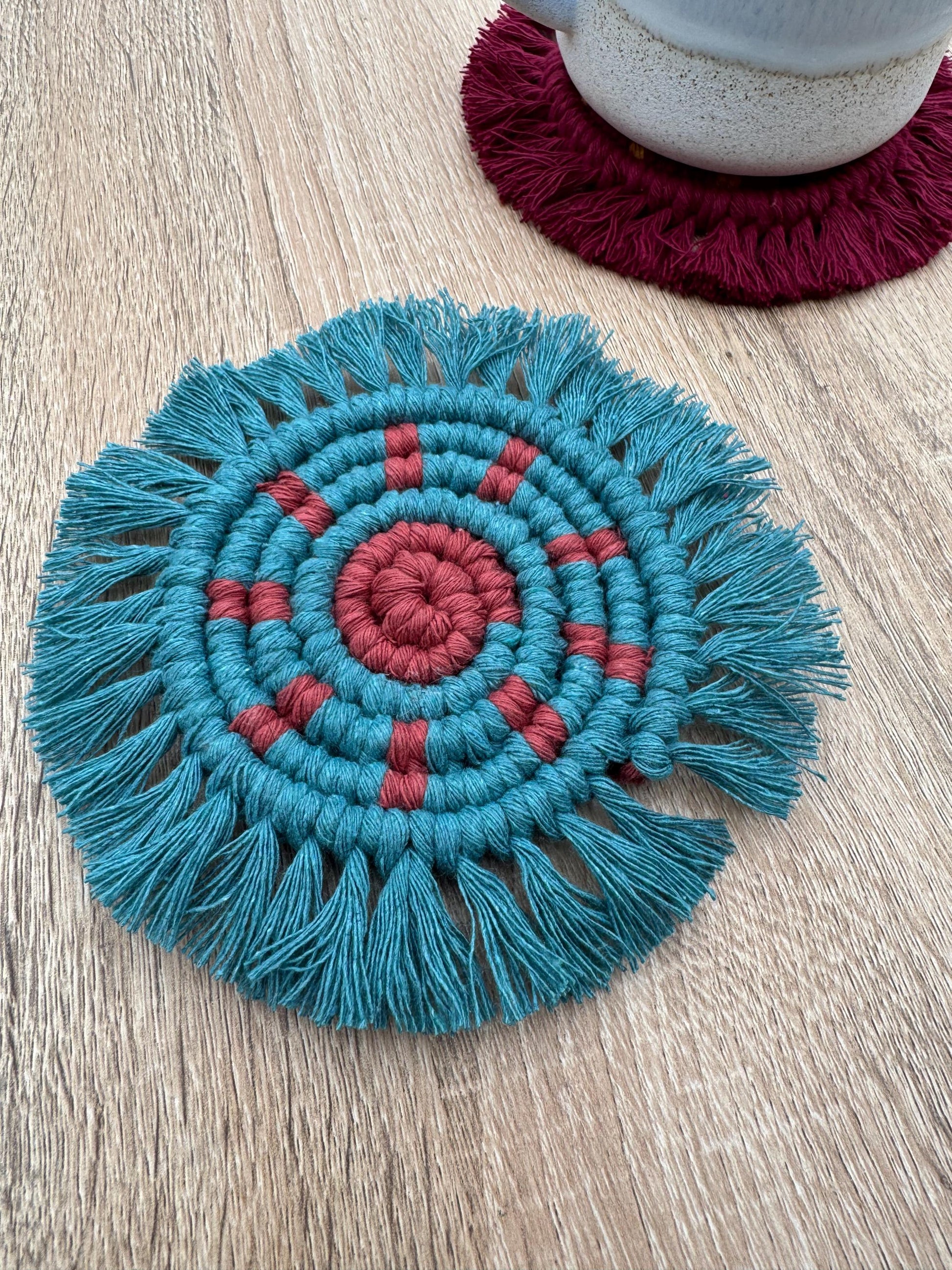 Teal and red macrame sun coaster on a wooden surface