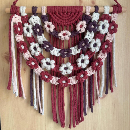 Burgundy macrame wall hanging with floral patterns on a wooden surface