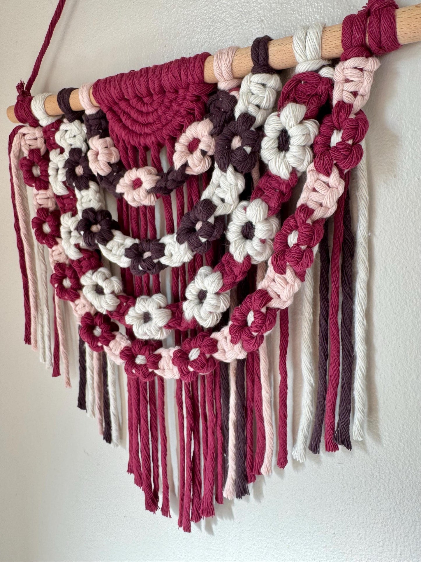 Macrame wall hanging with floral patterns in red, white, and brown on a plain background