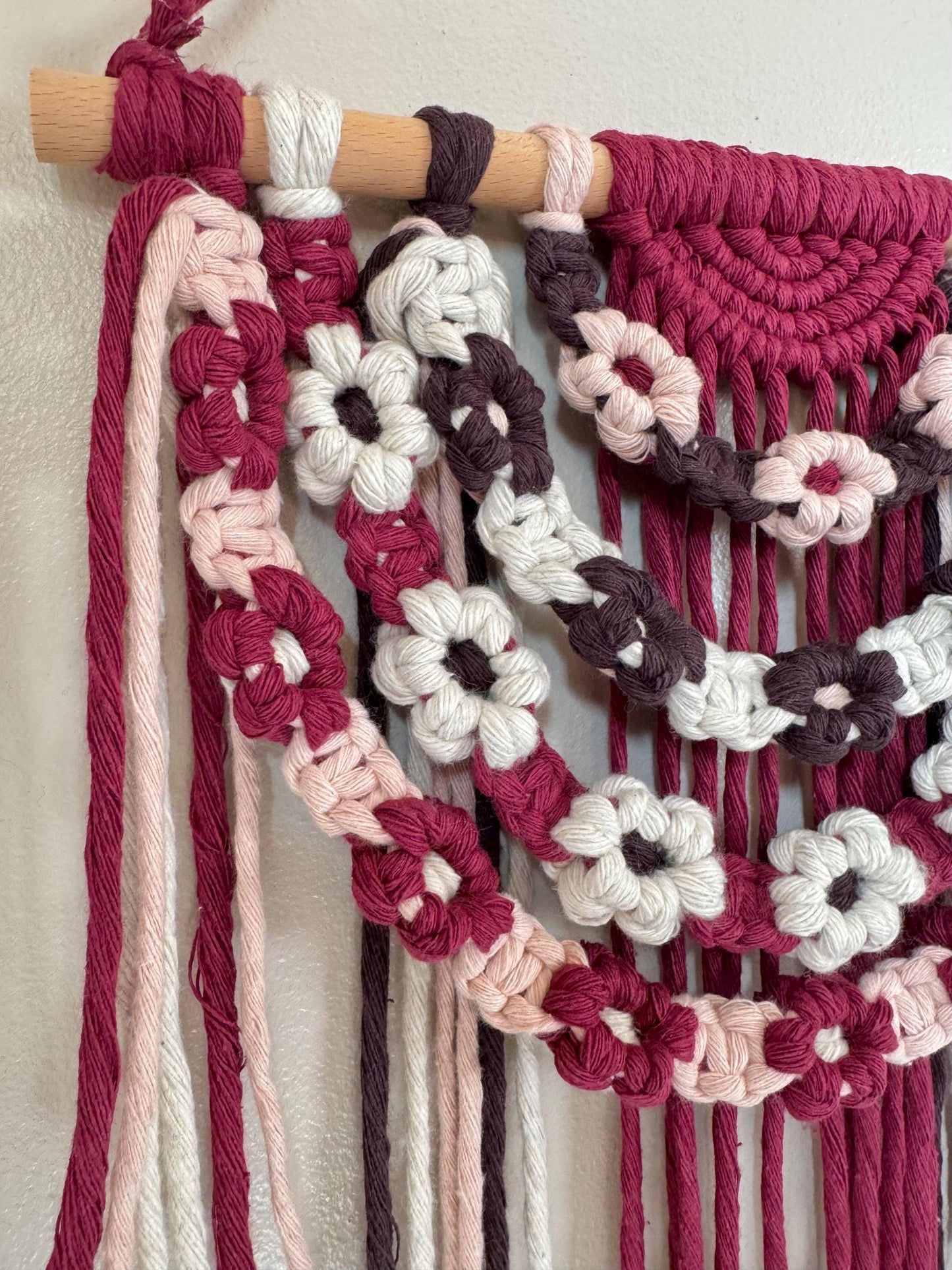 Macrame wall hanging with floral patterns in pink, white, and brown on a neutral background