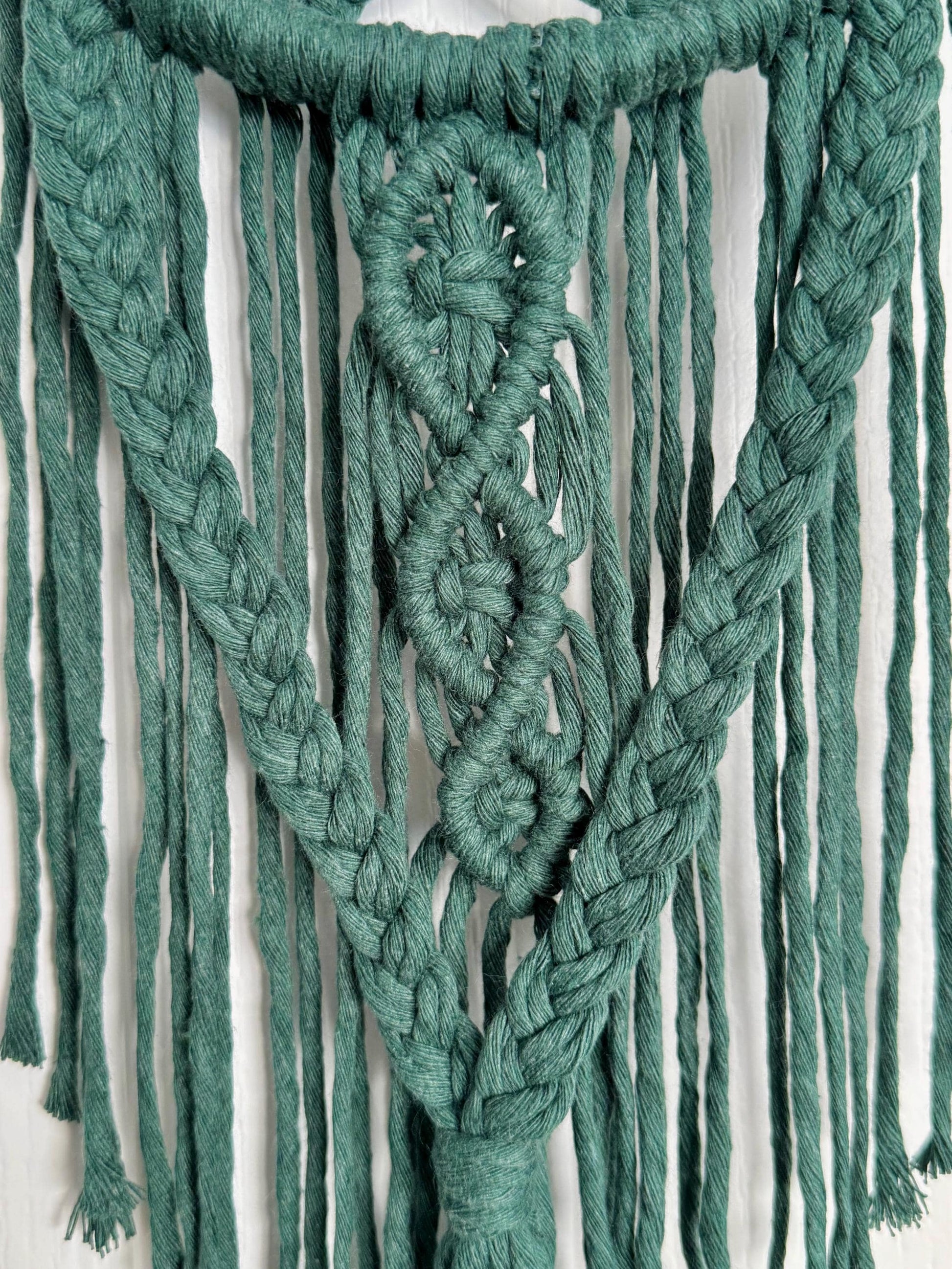 Green braided macrame wall hanging on a white background