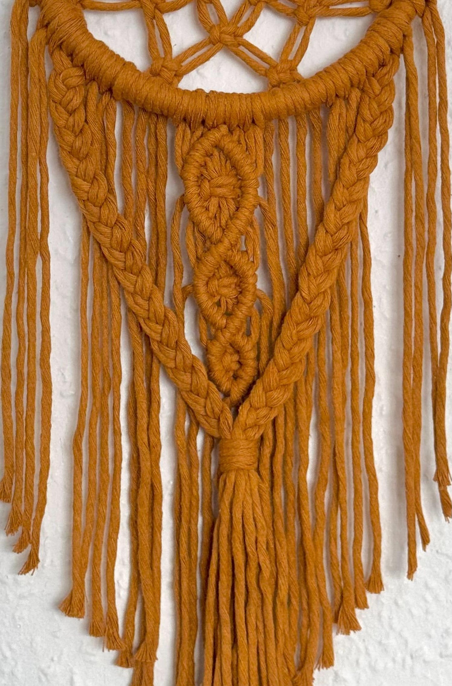 Mustard yellow macrame wall hanging on a textured white wall