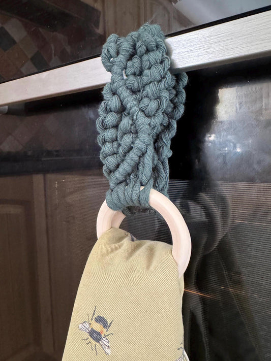 Green macrame attached to wooden rings, holding a yellow tea towel with a bee design