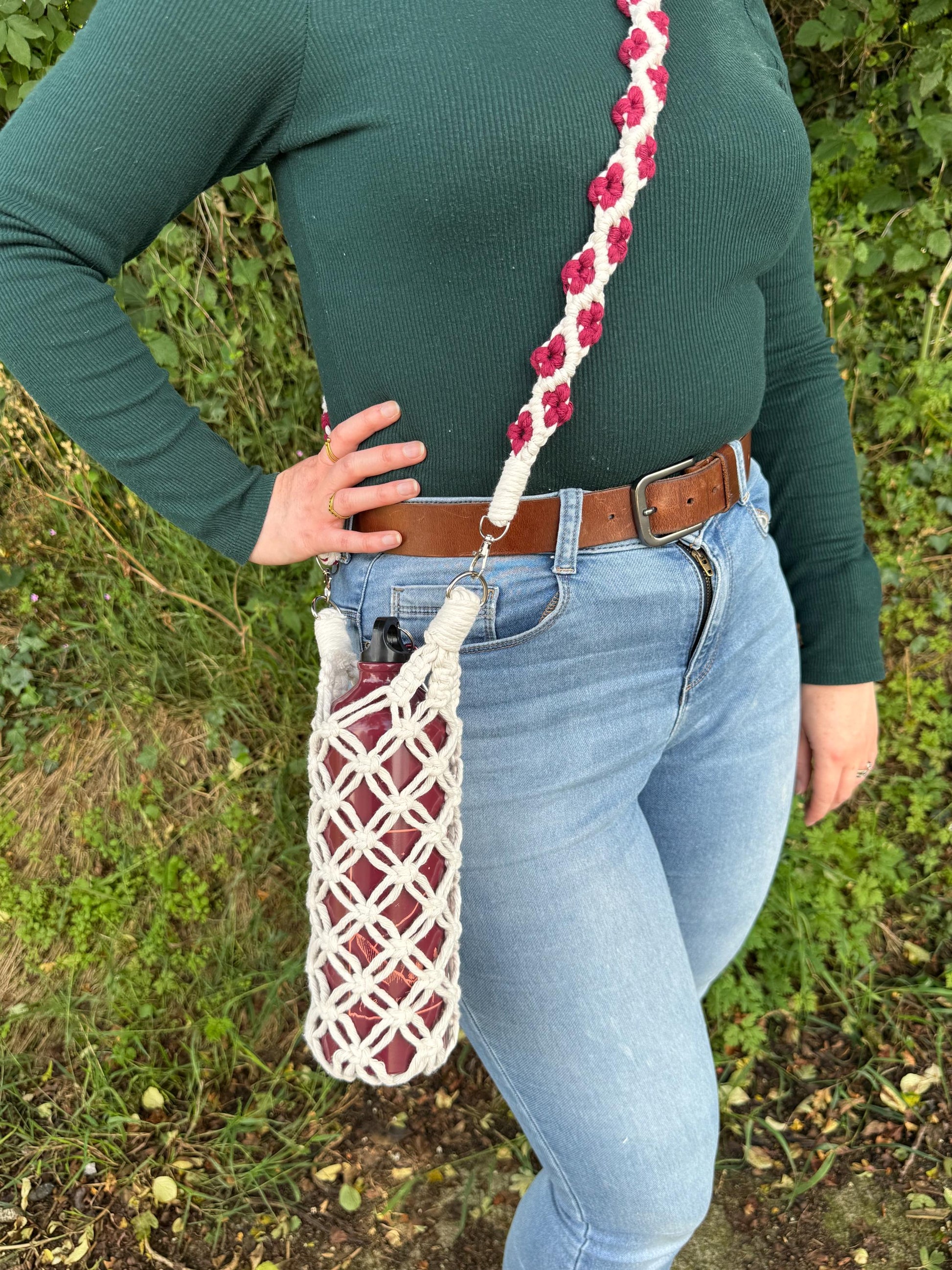 Person wearing a green sweater and blue jeans with a macrame water bottle bag on a grassy background