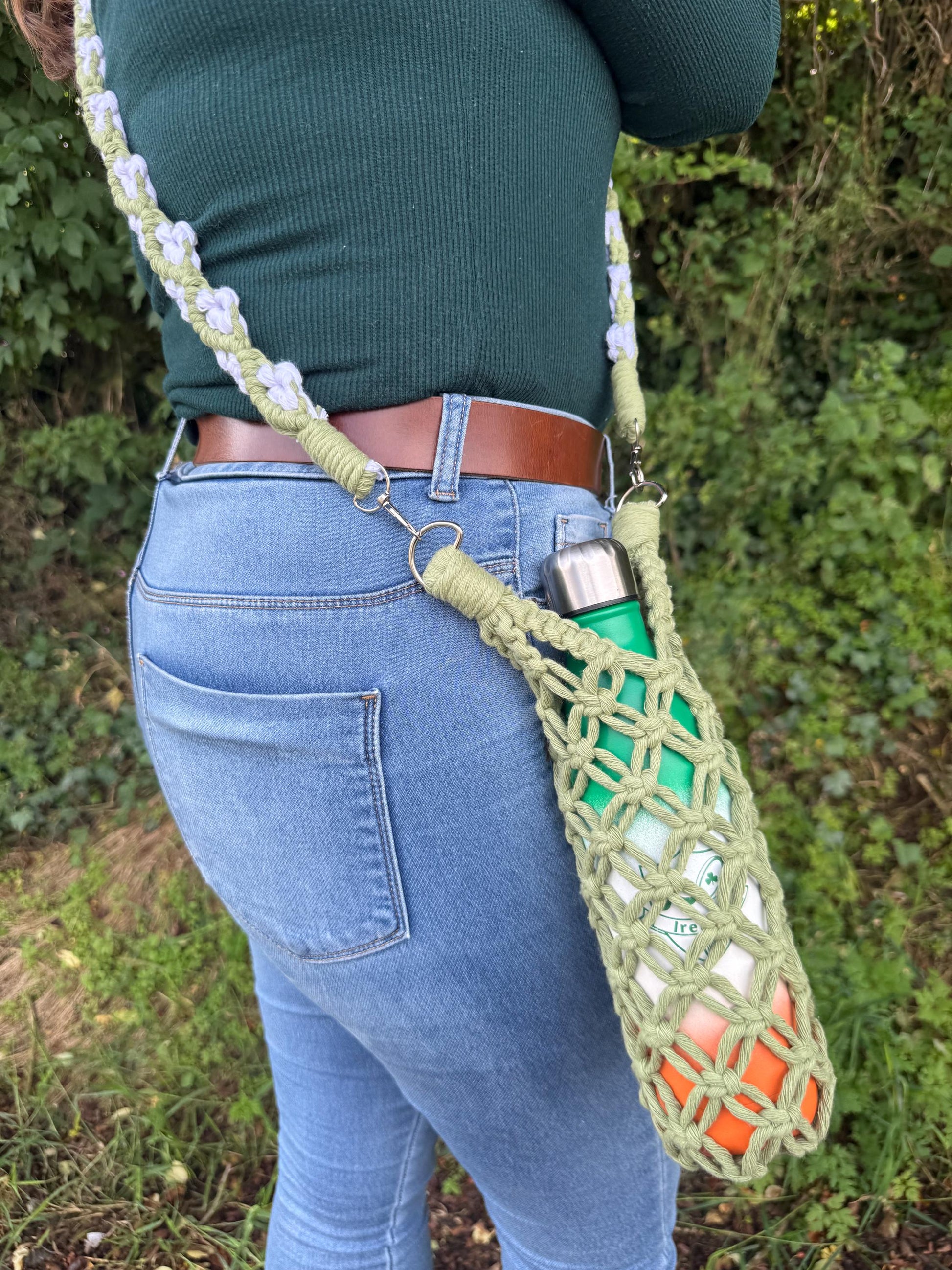 Person wearing a green macrame crossbody bag containing a water bottle, standing outdoors.