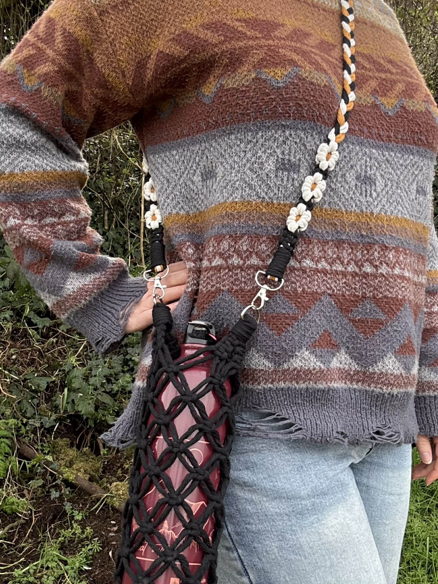 Person wearing a patterned sweater with a macrame bag over their shoulder outdoors.