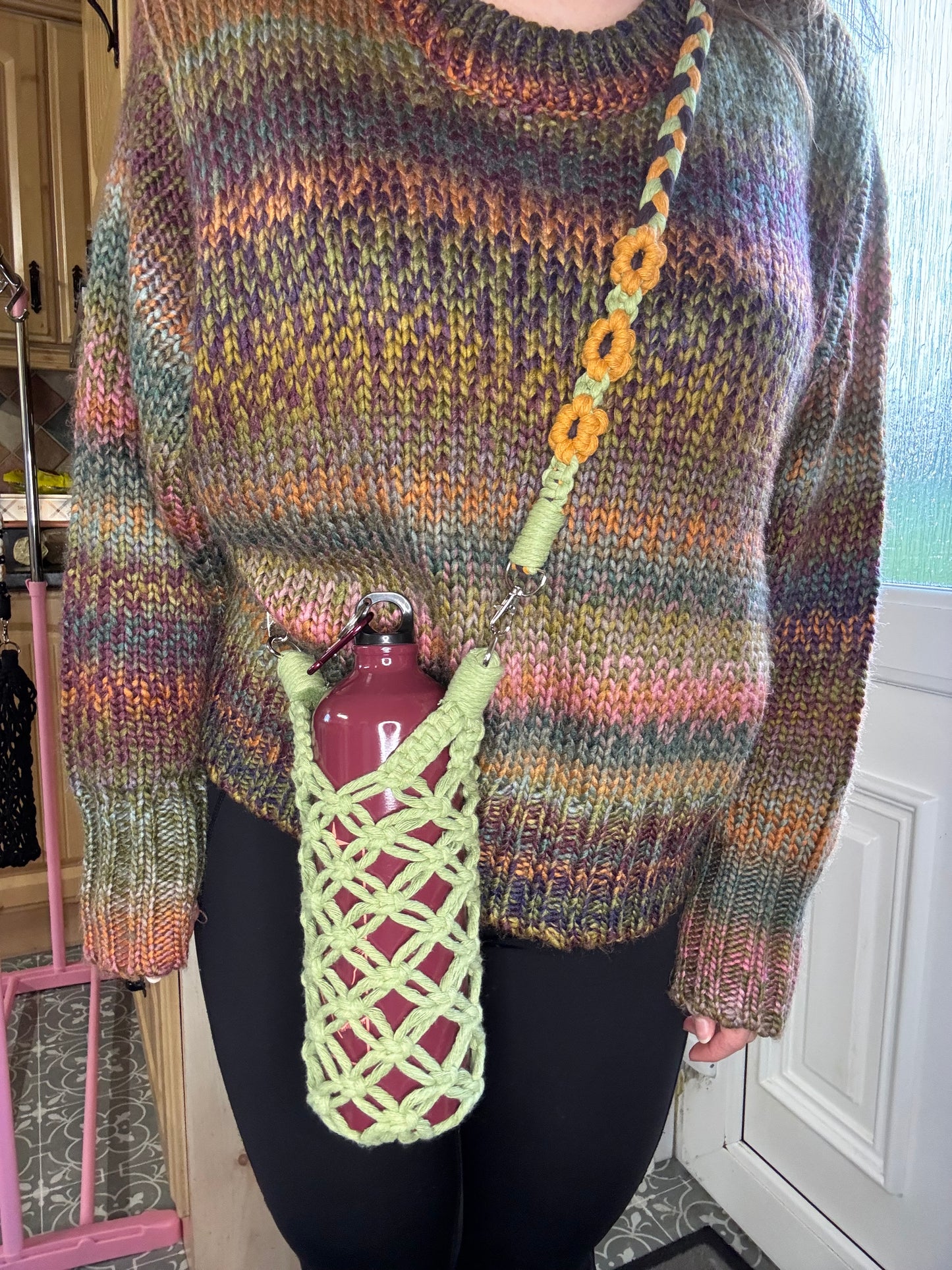 Person wearing a colorful knitted sweater with a green mesh water bottle bag over their shoulder.