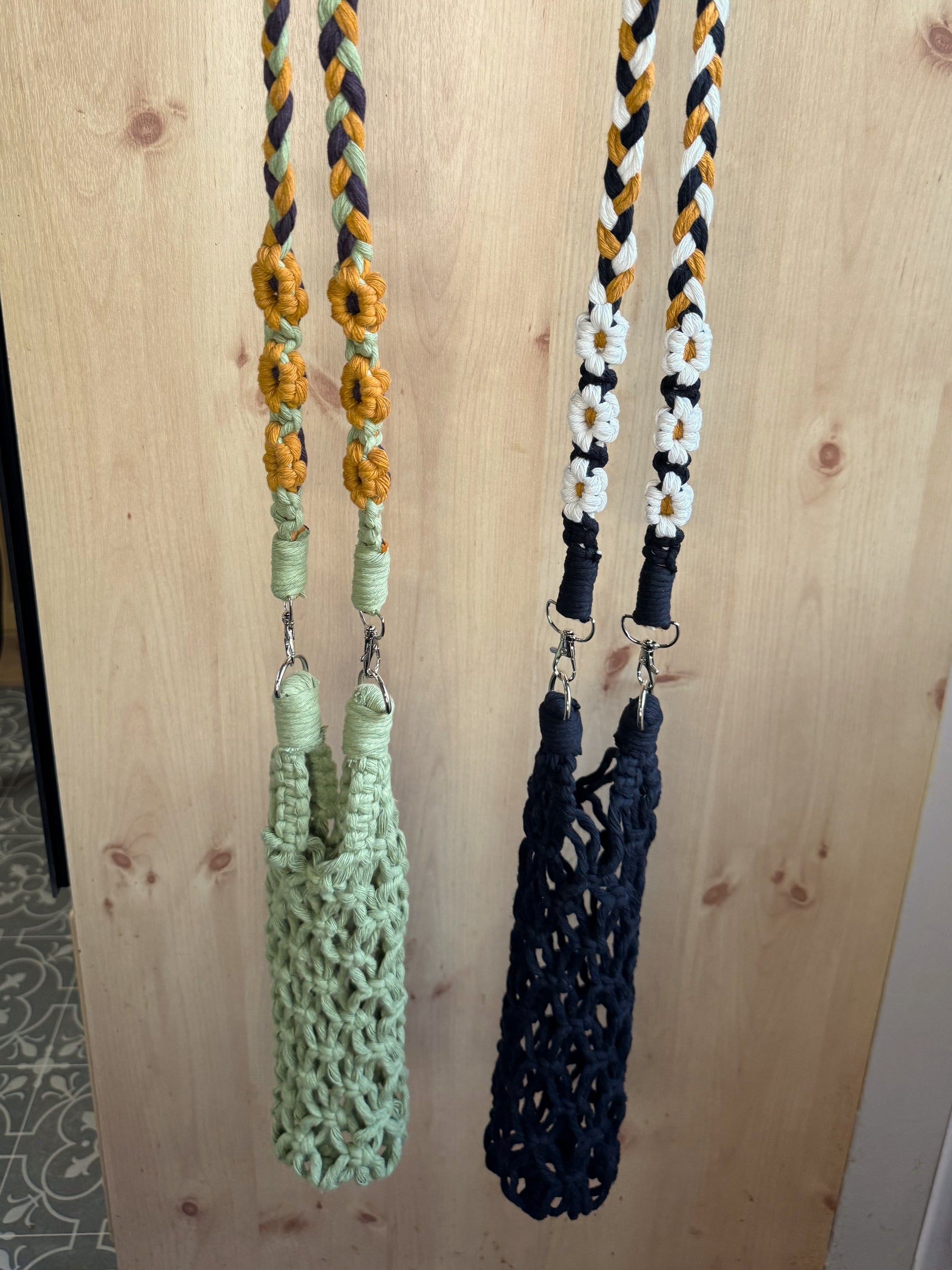 Two floral macrame net bags, one green and one black , hanging on a wooden surface.