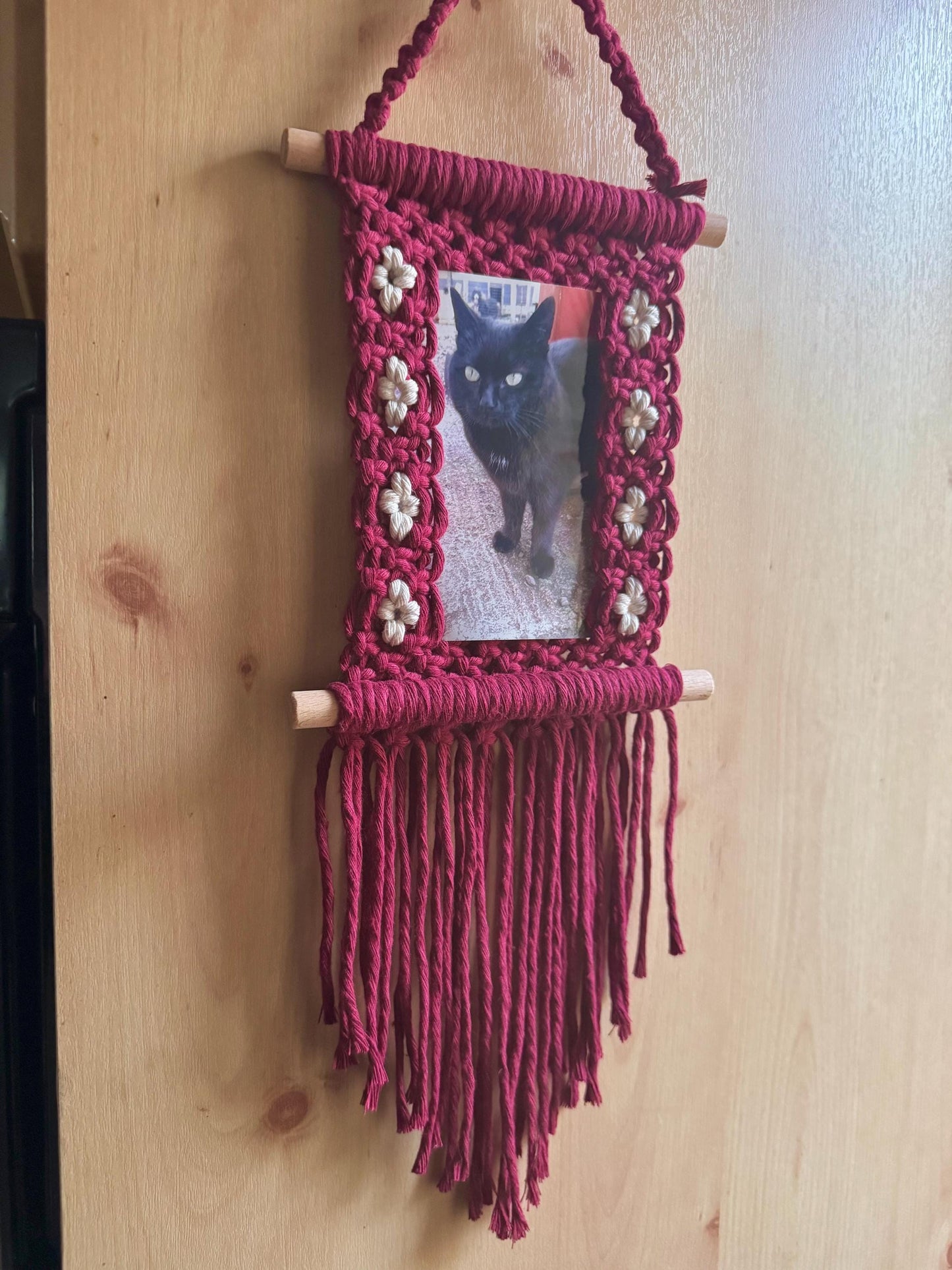 Macrame hanging frame with a photo of a black cat on a wooden surface