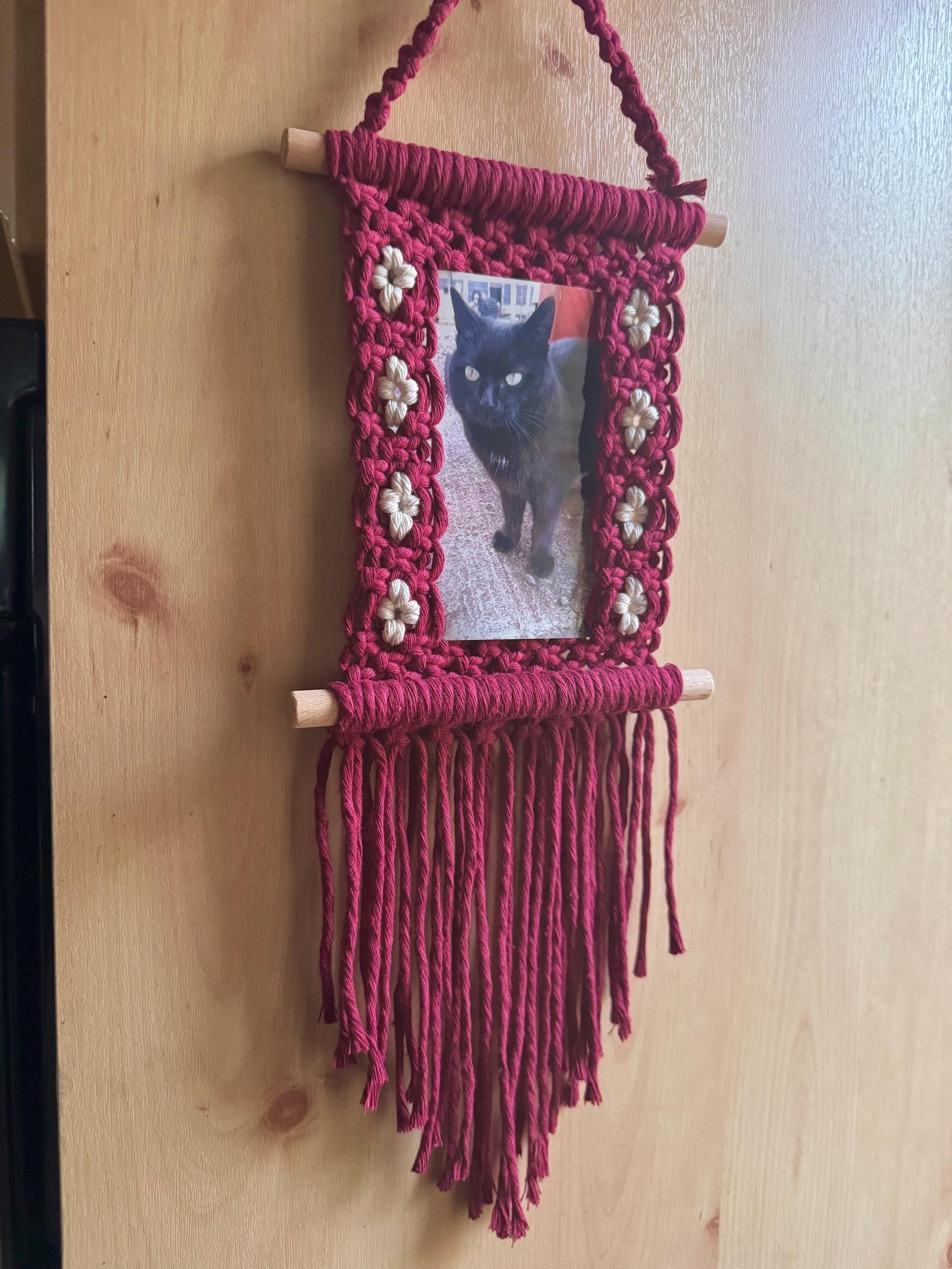 Macrame hanging frame with a photo of a black cat on a wooden surface
