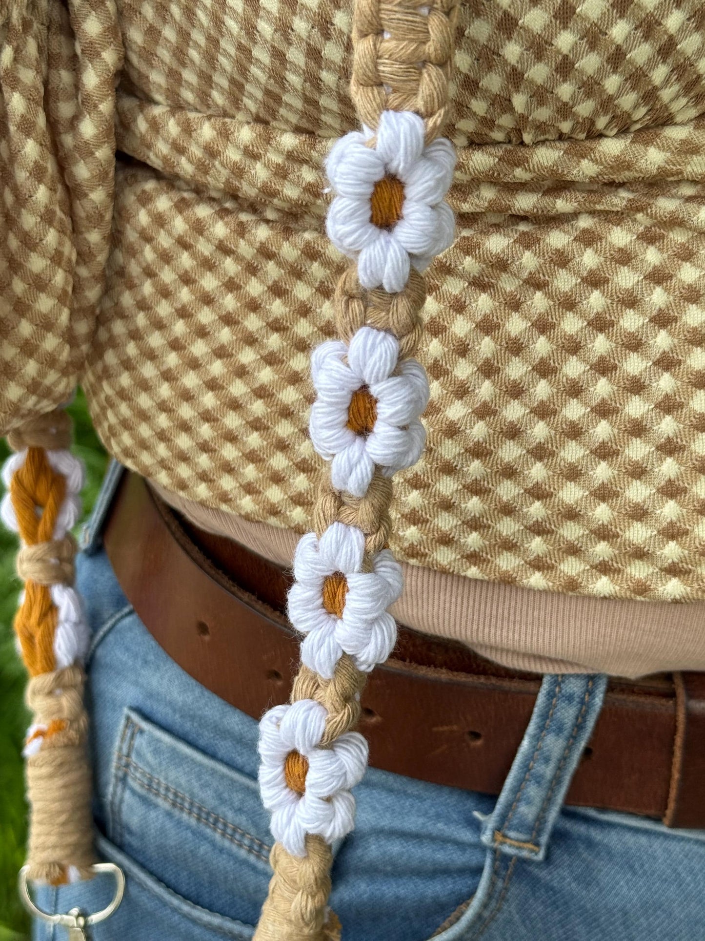 Close-up of a macrame strap with floral patterns worn by a person in a checkered shirt and jeans.