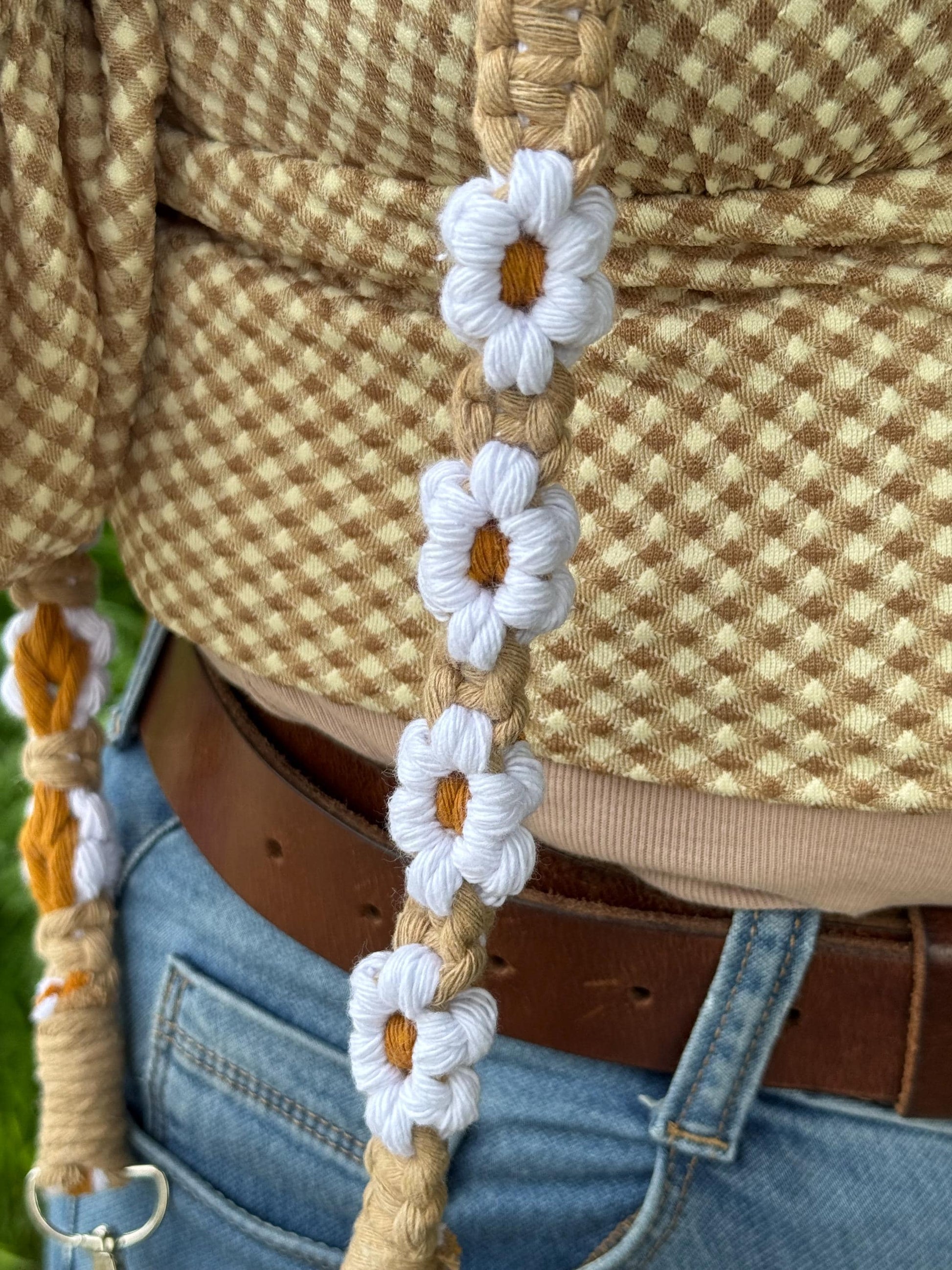 Close-up of a macrame strap with floral patterns worn by a person in a checkered shirt and jeans.