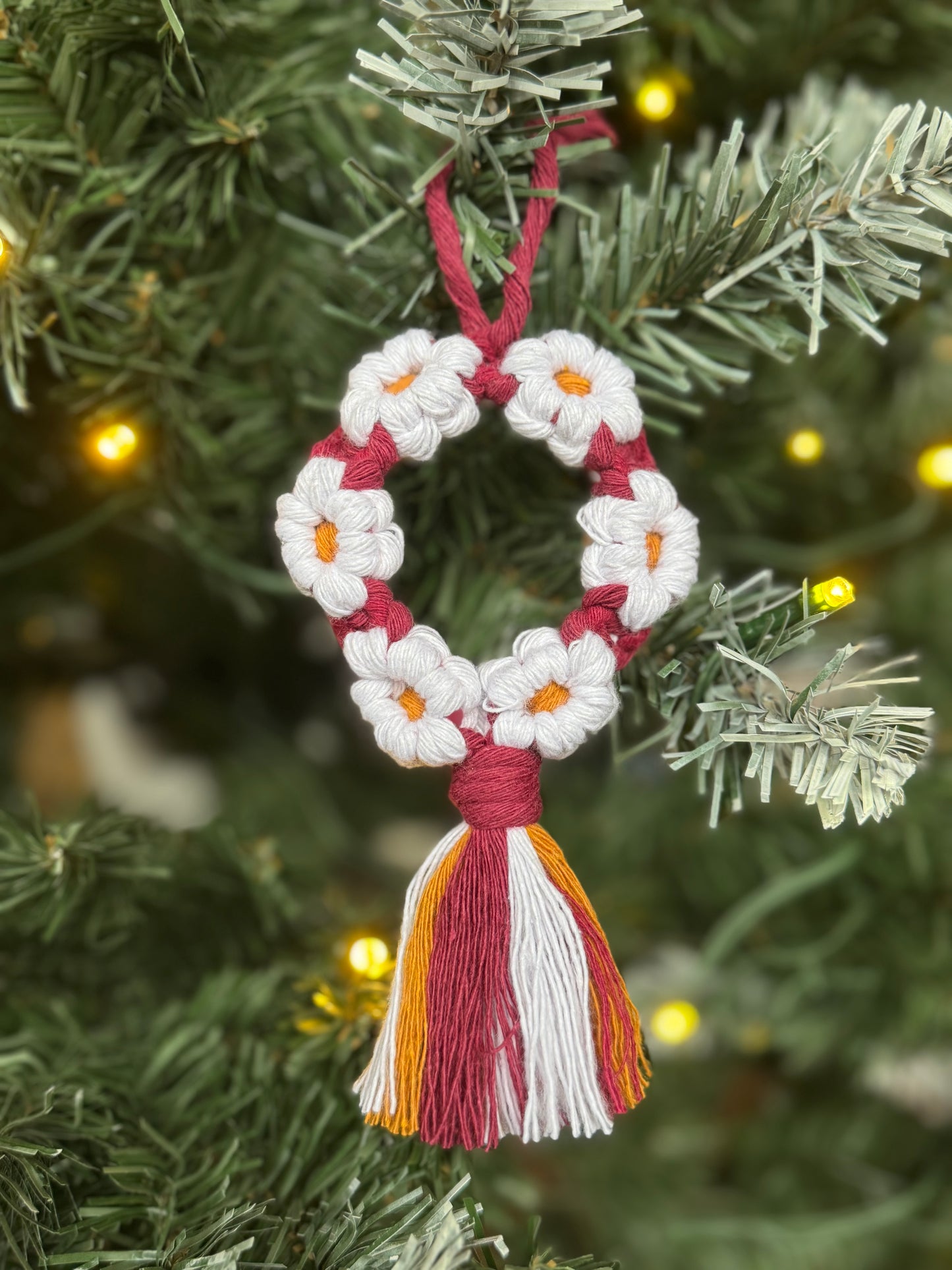 Decorative ornament with white flowers and red tassel on a Christmas tree.