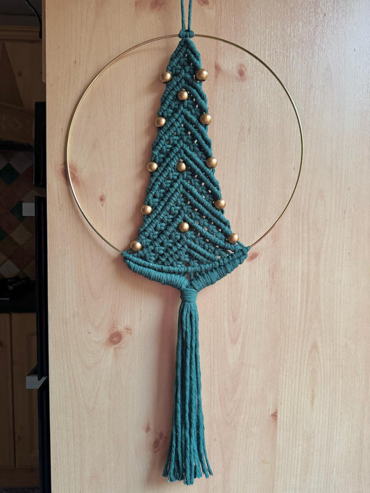 Dark green macrame Christmas tree wall hanging with gold beads on a wooden surface