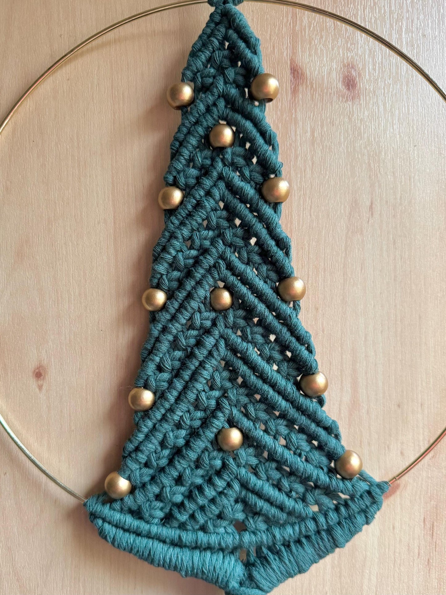 Dark green macrame christmas tree wall hanging with gold beads on a wooden surface